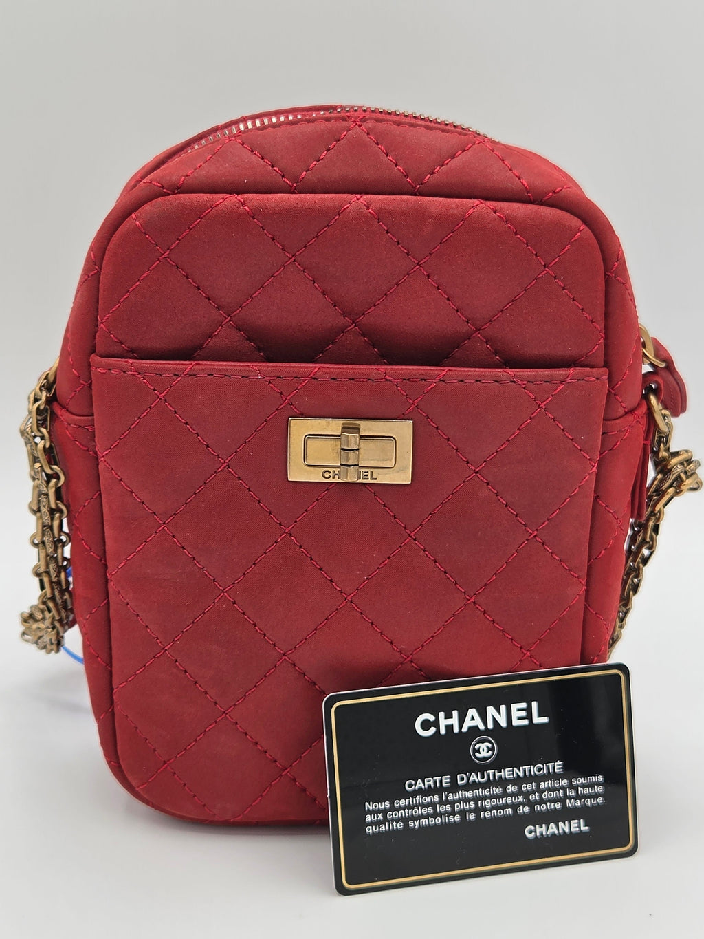 Red quilted handbag with gold chain strap and Chanel tag on a light gray background