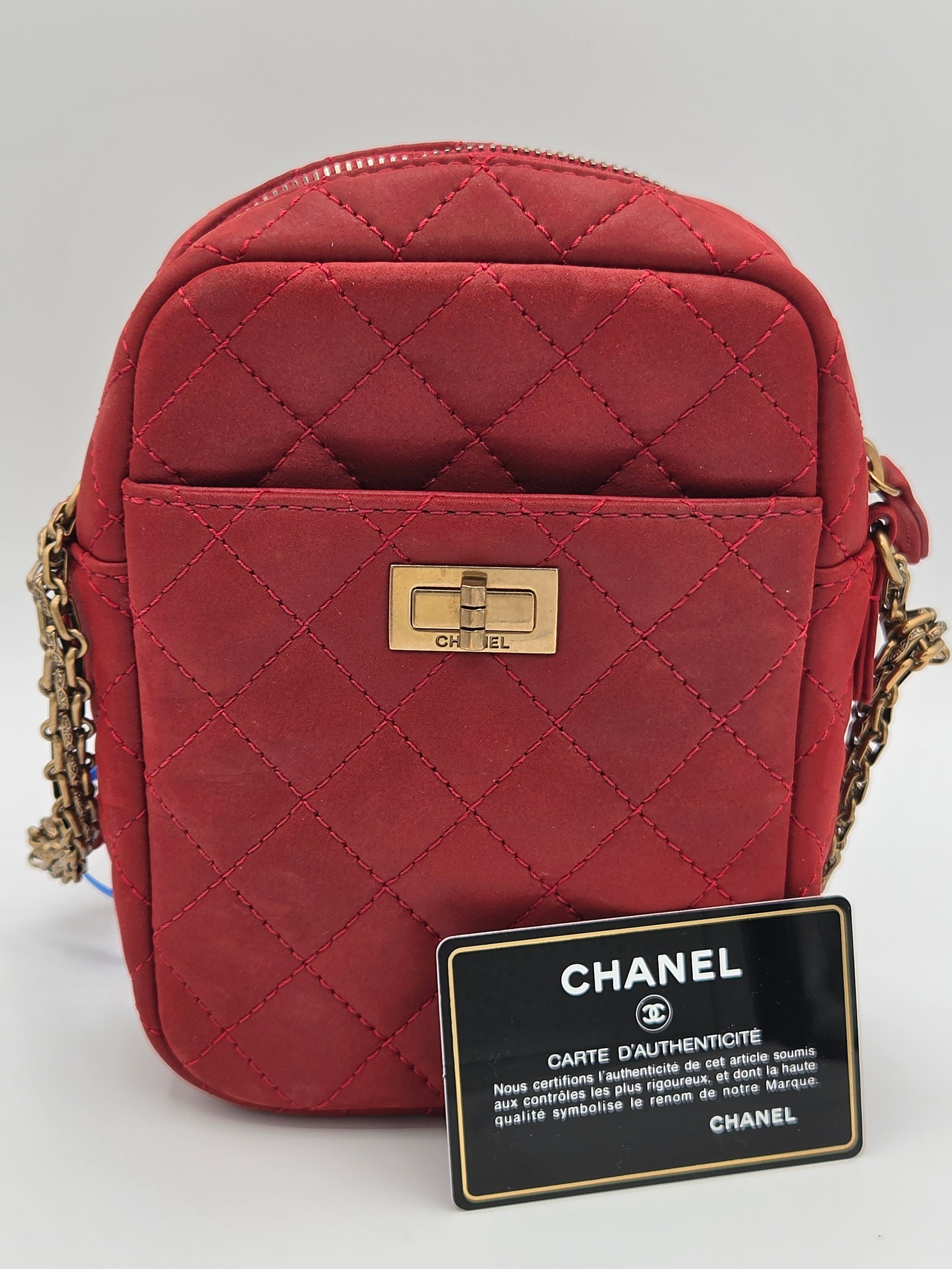 Red quilted handbag with gold chain strap and Chanel tag on a light gray background