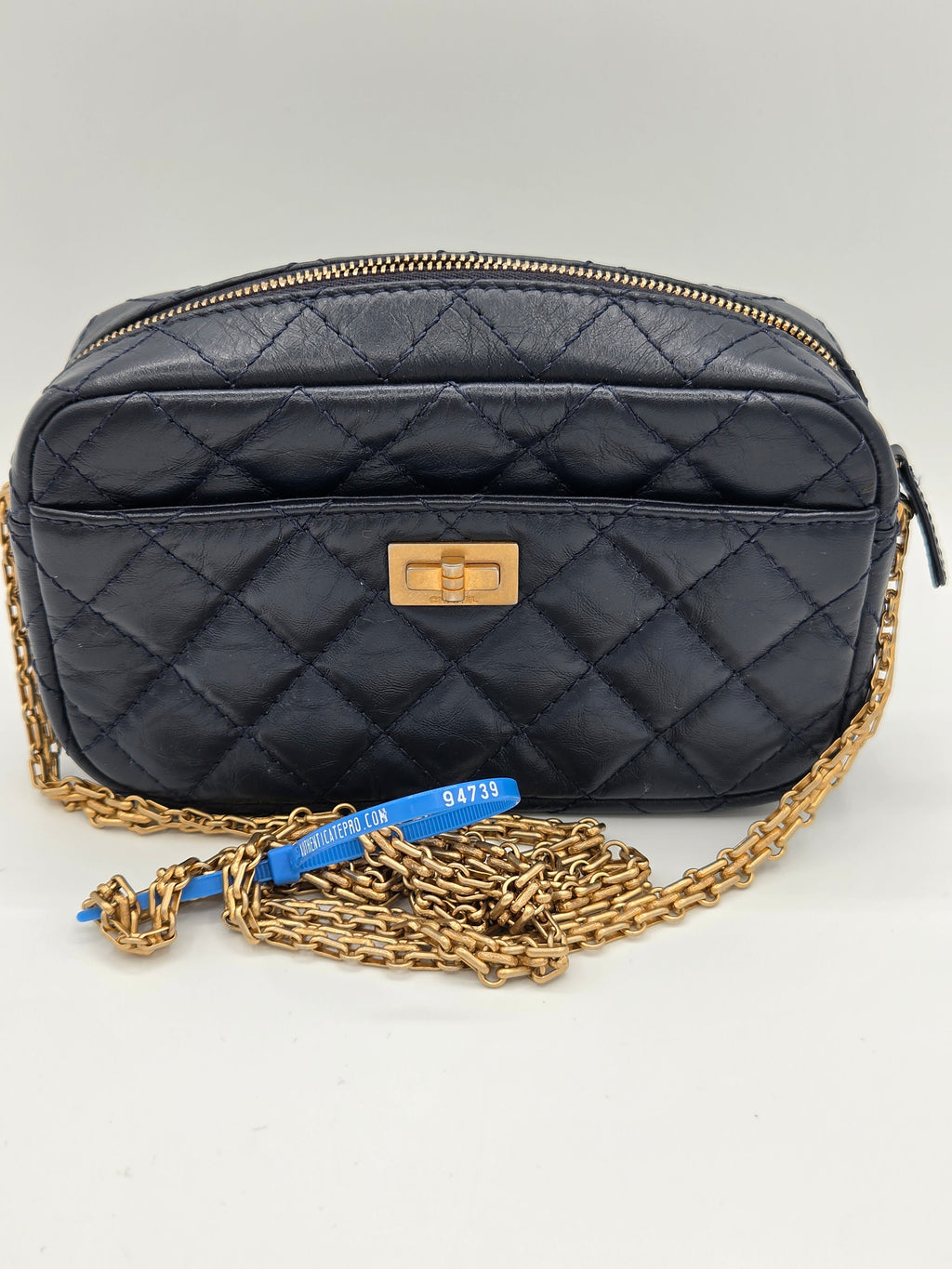 Black quilted handbag with gold chain strap on a light gray background