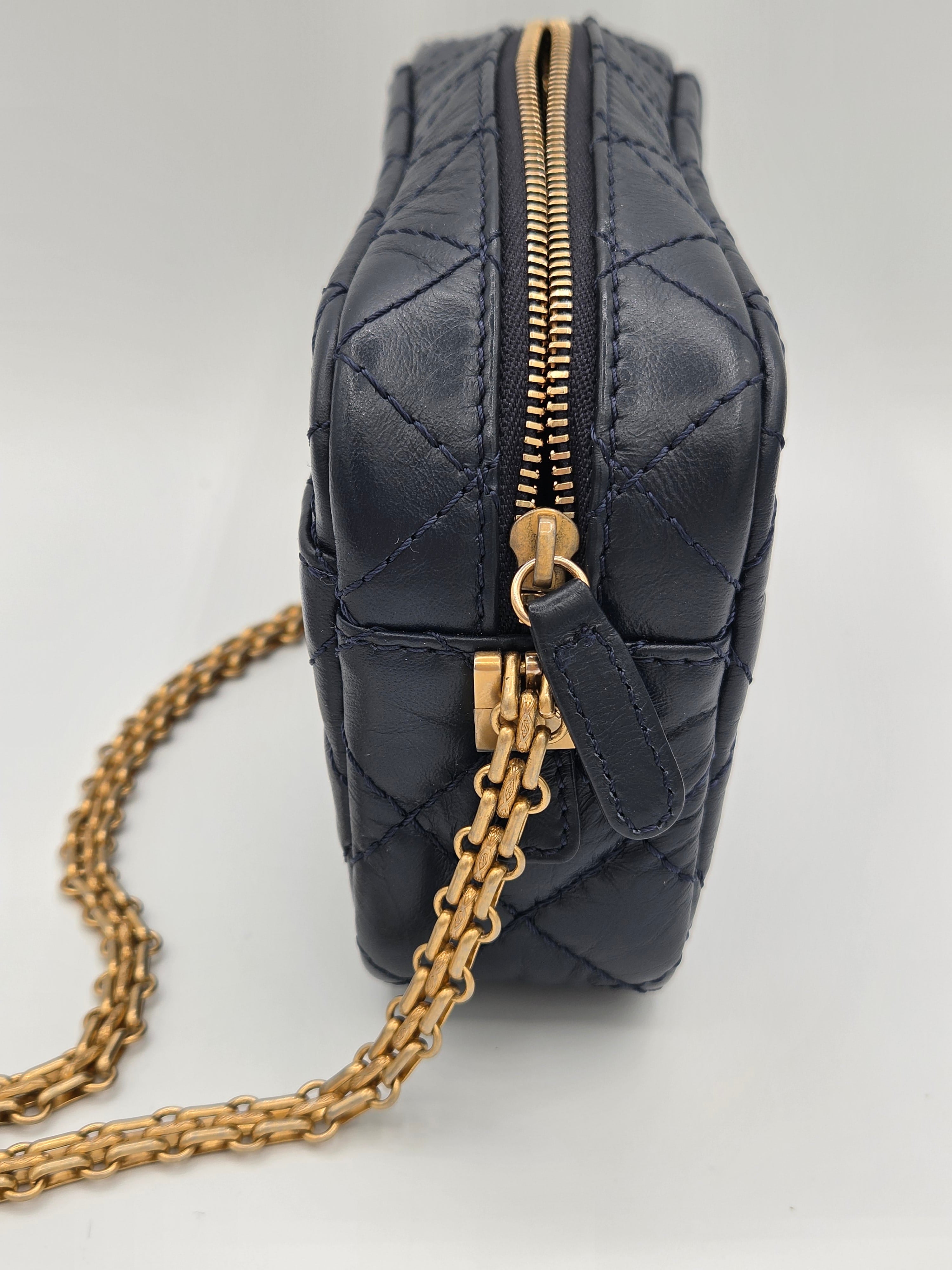 Black quilted handbag with gold chain strap on a light gray background