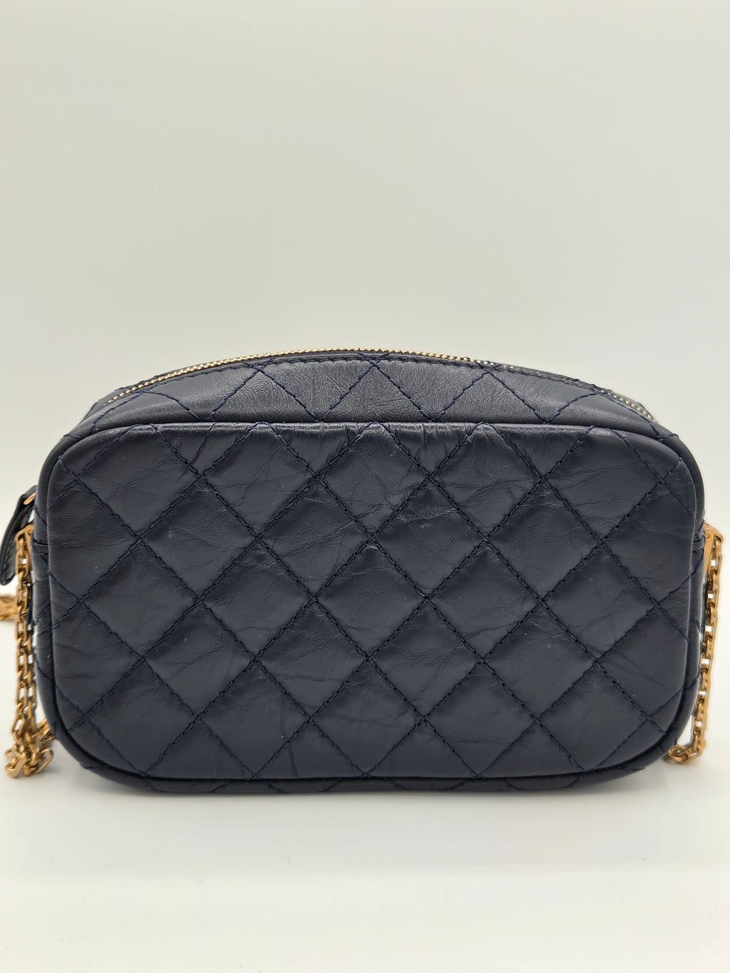 Quilted black handbag with gold chain on a light gray background