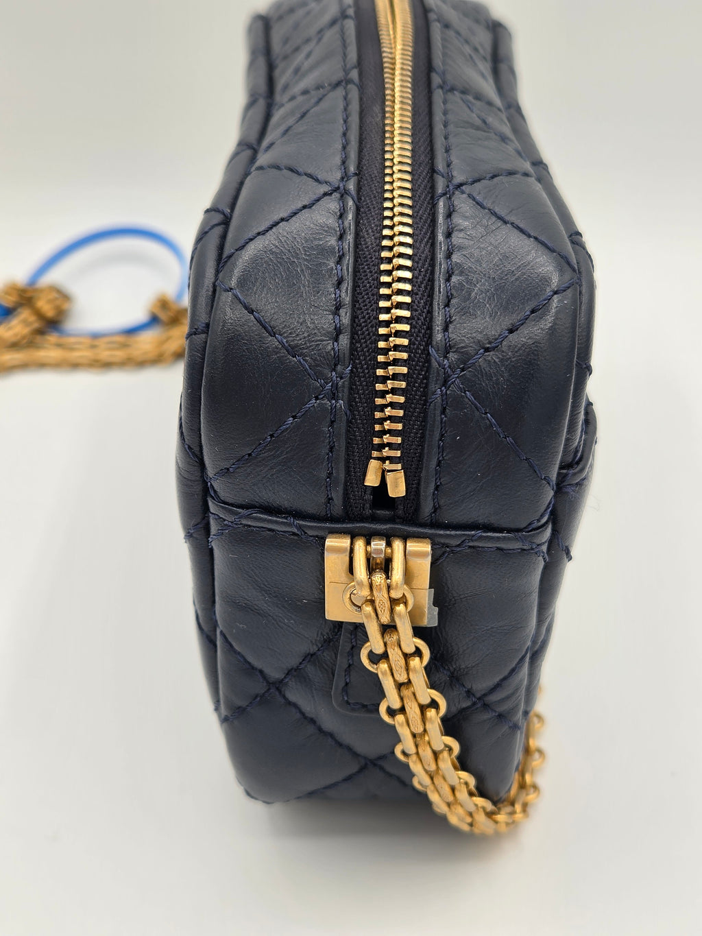 Black quilted bag with gold zipper and chain detail on a light gray background