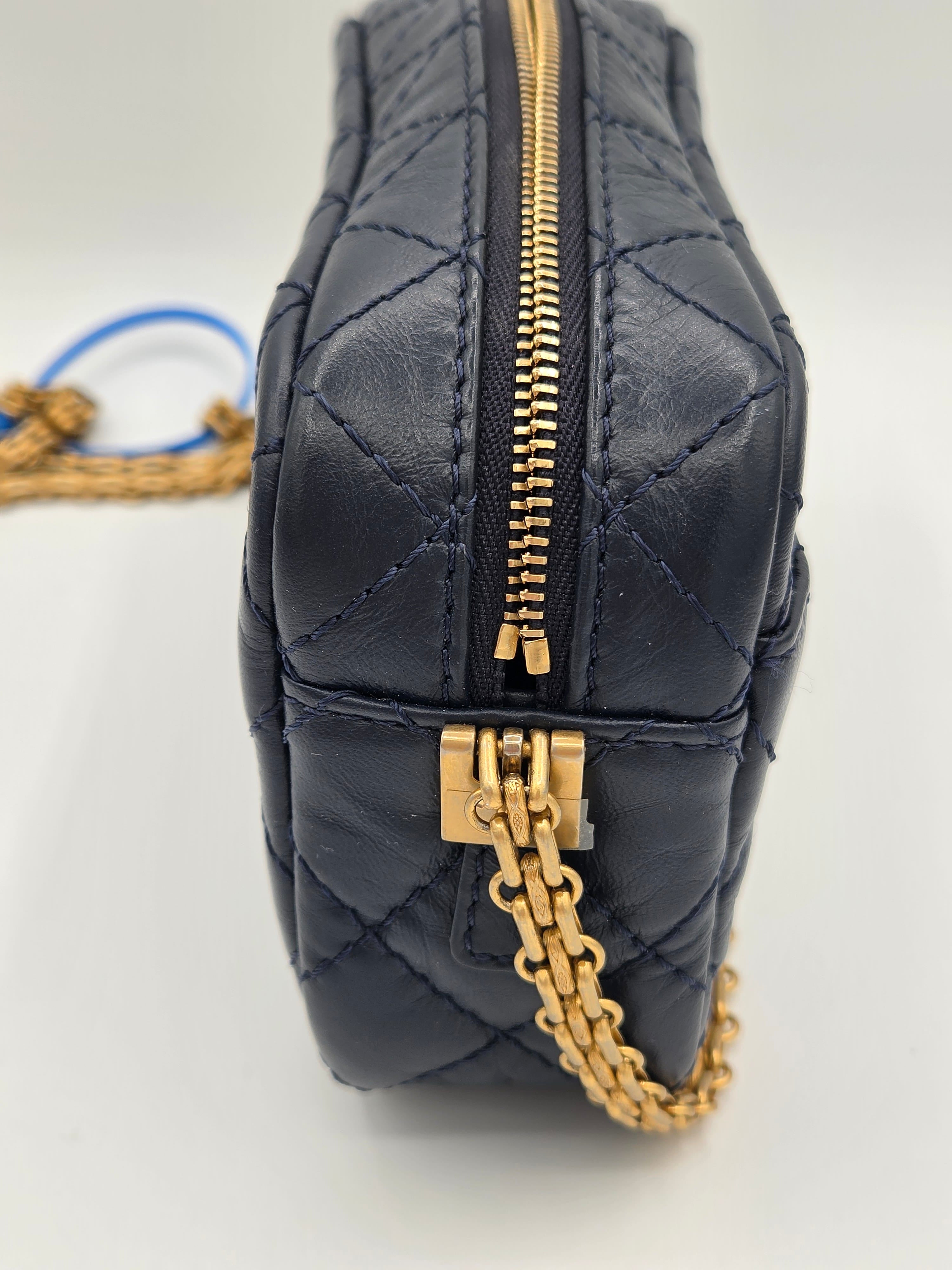Black quilted bag with gold zipper and chain detail on a light gray background