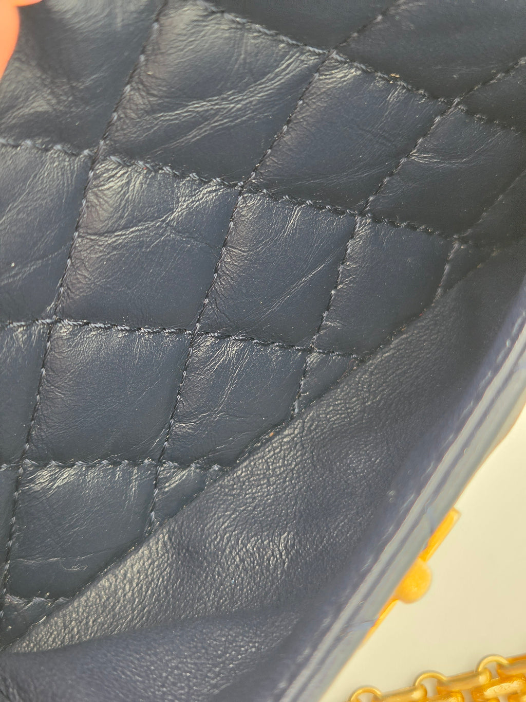 Close-up of a quilted dark blue leather handbag with a gold chain handle.