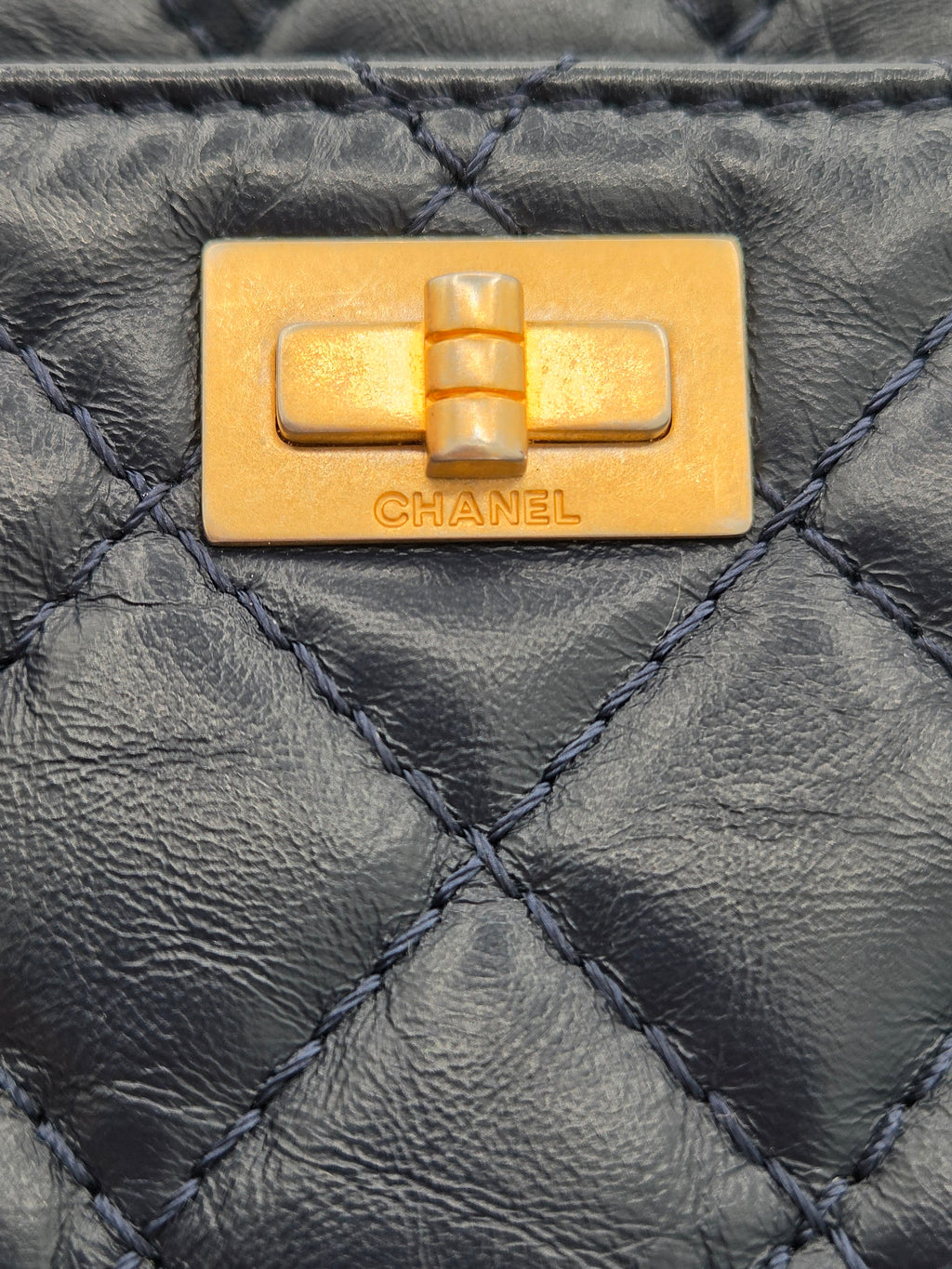 Close-up of a Chanel gold turnlock on a black quilted leather bag.