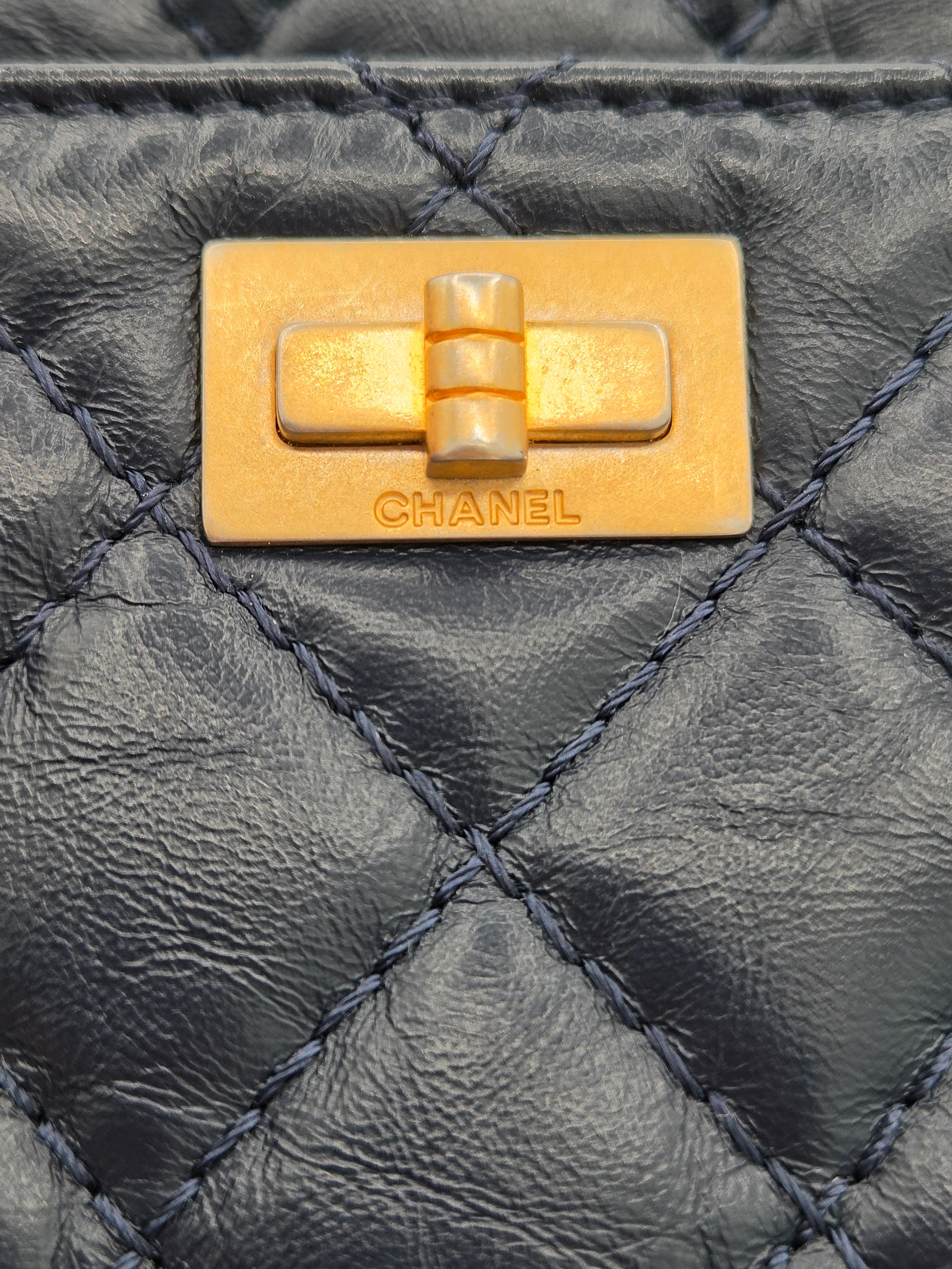 Close-up of a Chanel gold turnlock on a black quilted leather bag.