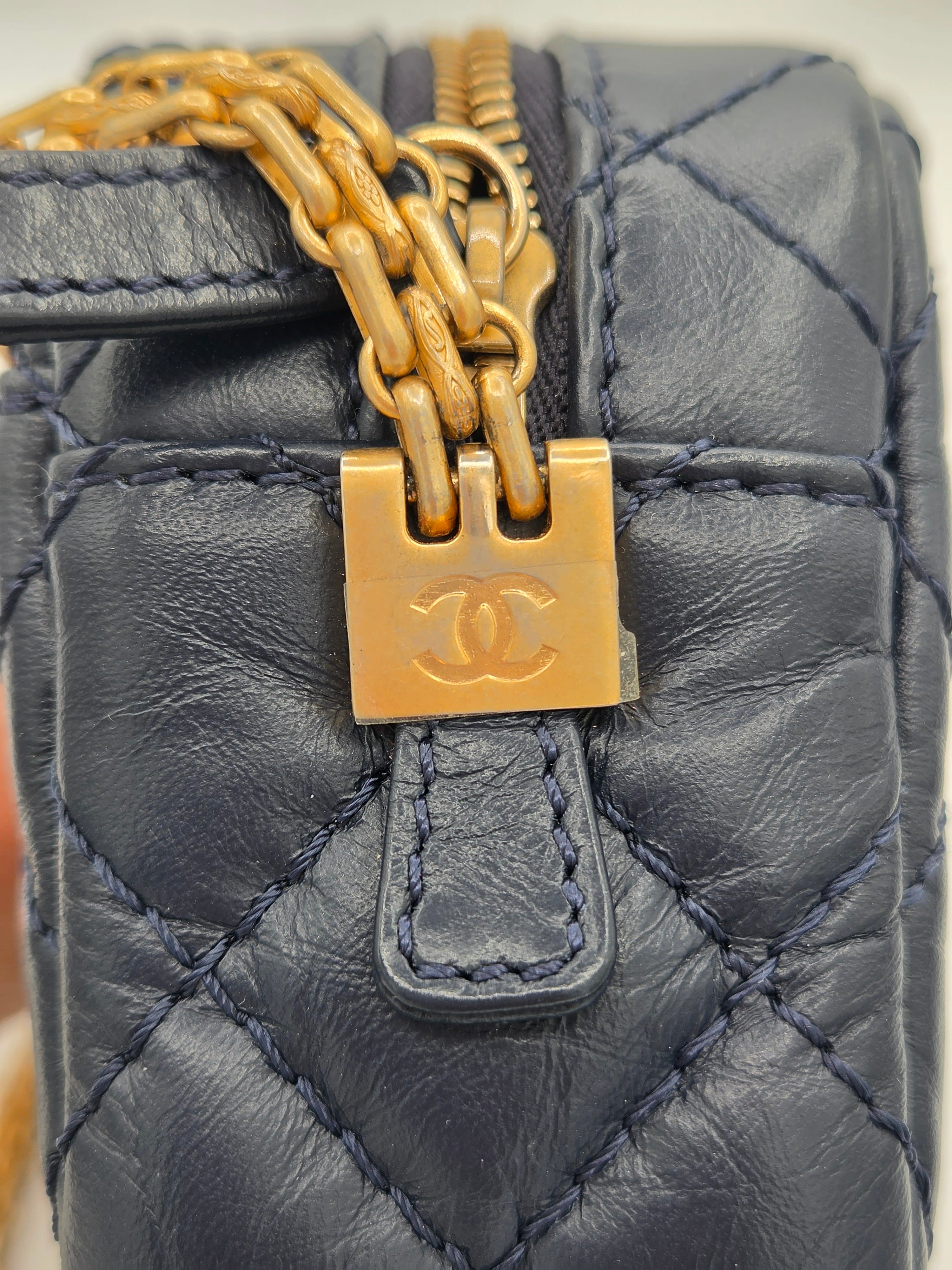 Close-up of a quilted handbag with a gold chain and clasp, featuring the Chanel logo.