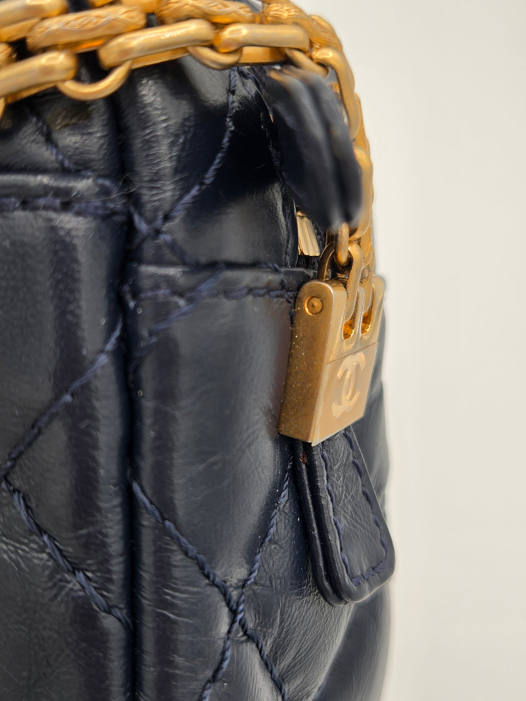 Close-up of a black quilted handbag with gold chain and clasp on a light gray background