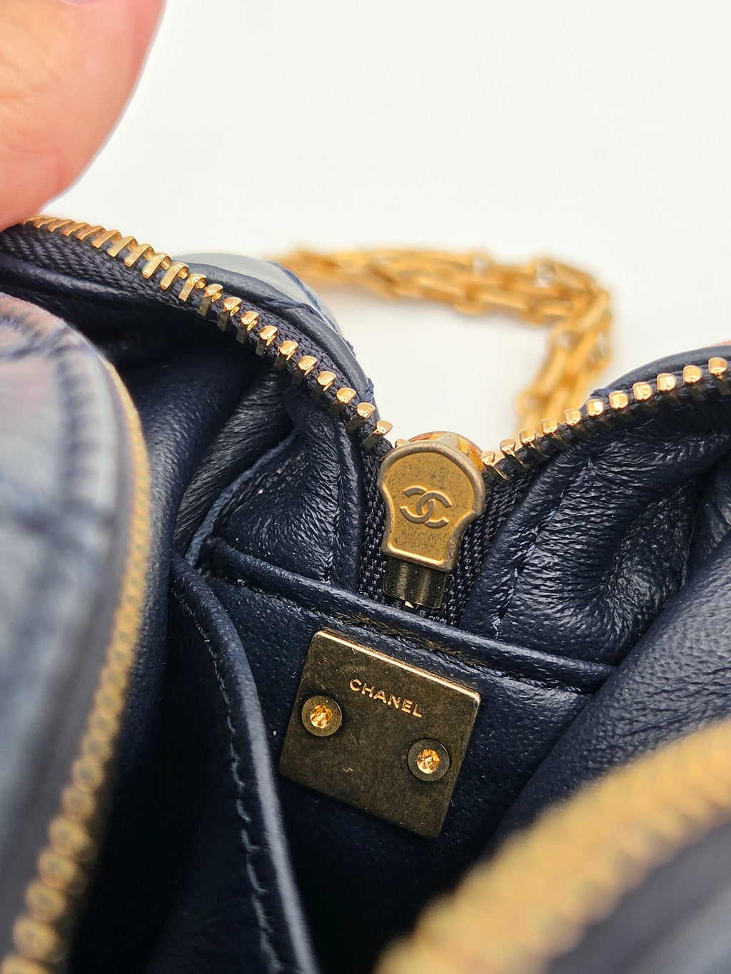 Close-up of a navy blue leather handbag with gold hardware, featuring the Chanel logo.