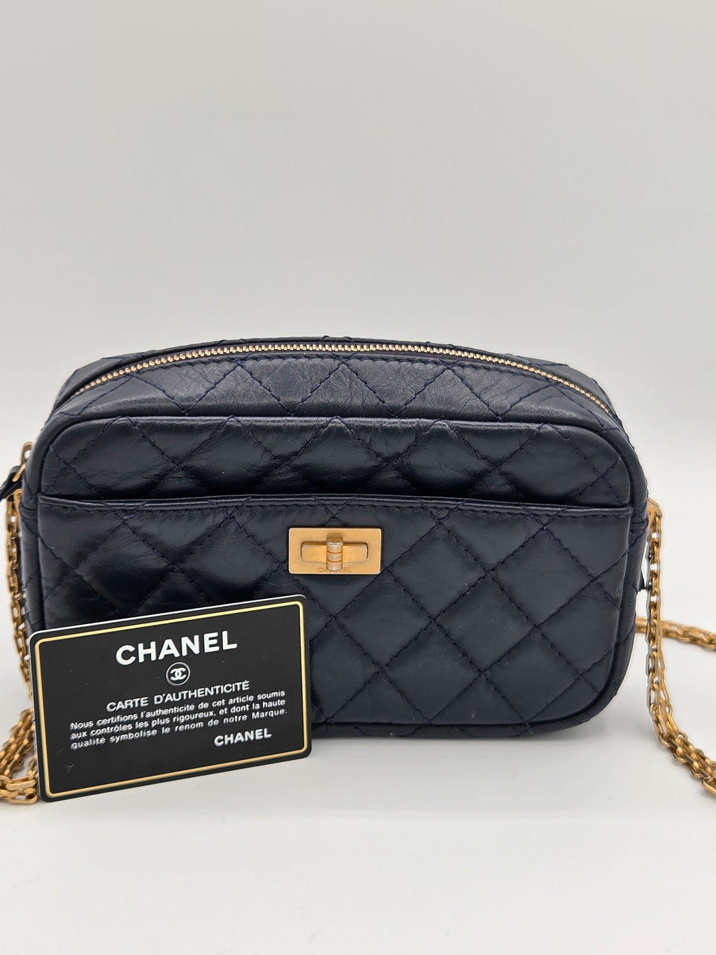 Black quilted Chanel handbag with gold chain on a light gray background