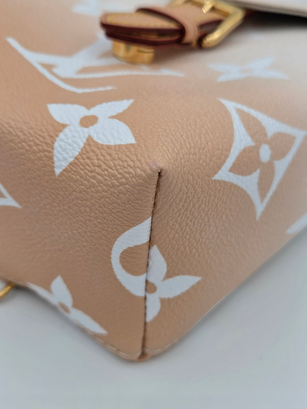 Close-up of a beige leather pouch with white monogram pattern on a light gray background