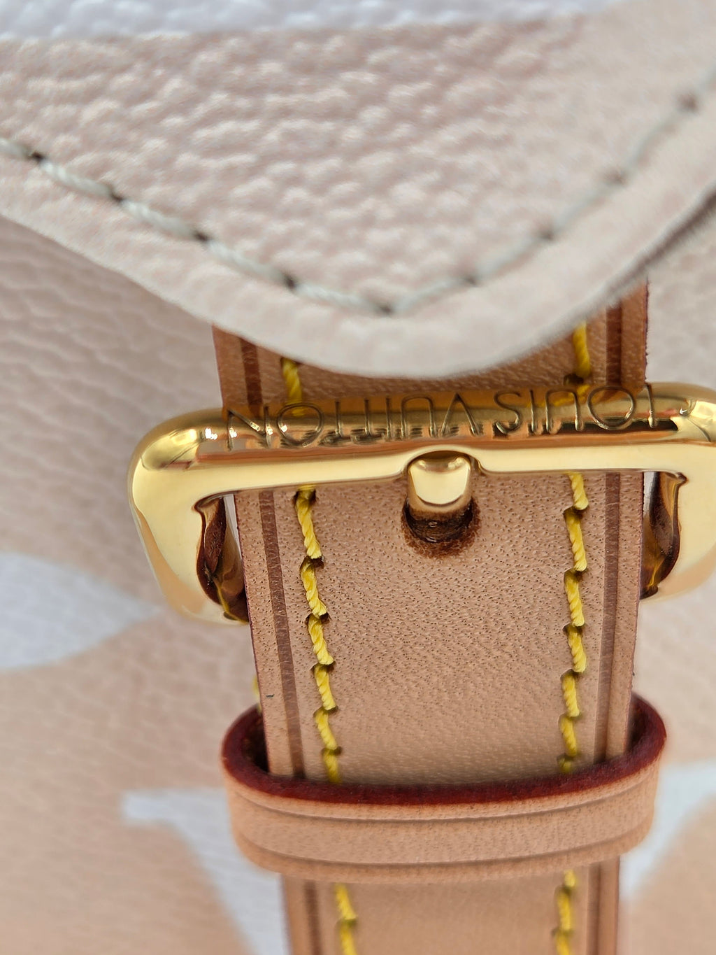 Close-up of a beige leather strap with gold buckle on a textured beige background
