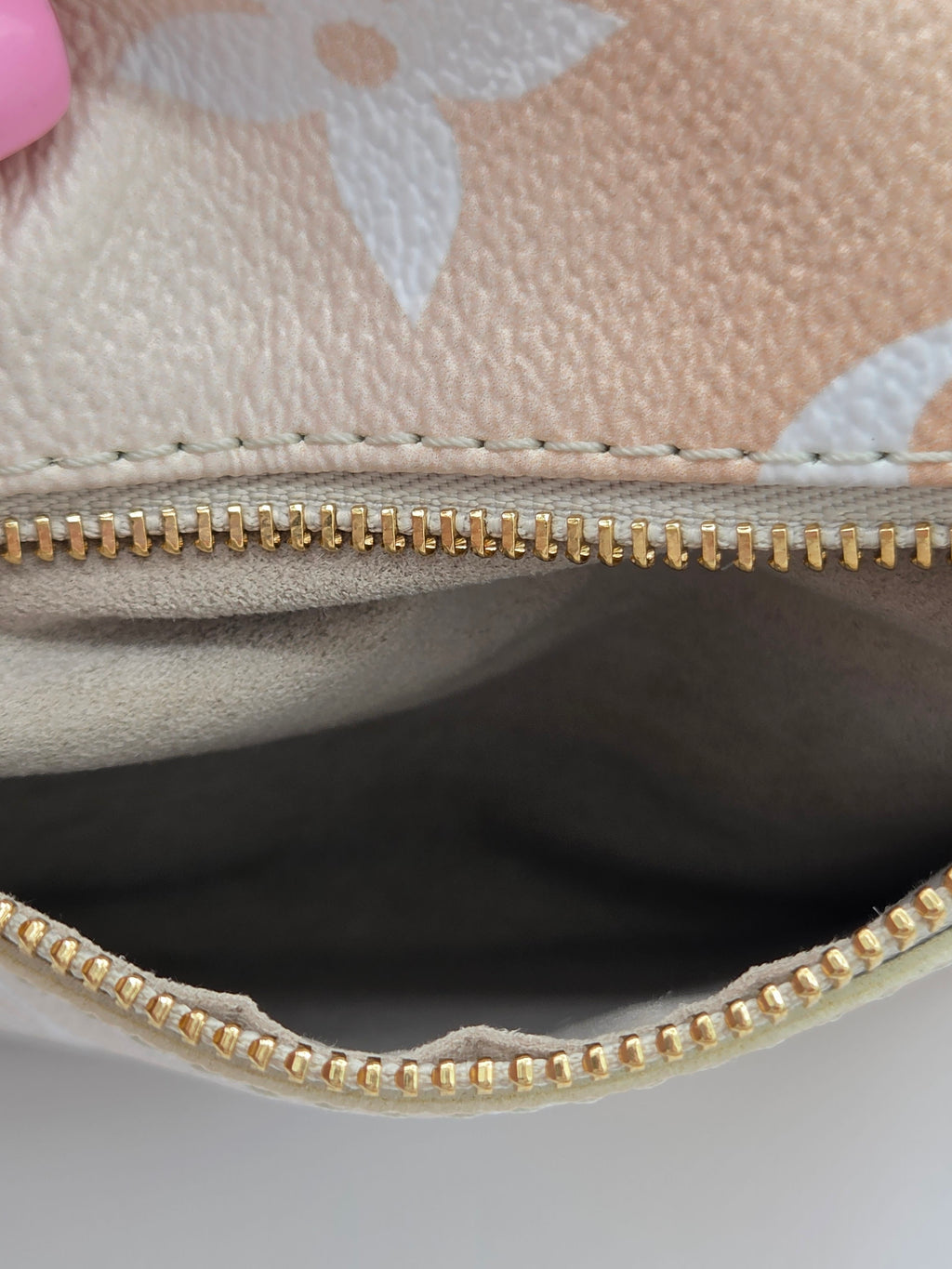 Close-up of a beige handbag with floral patterns and a gold zipper.