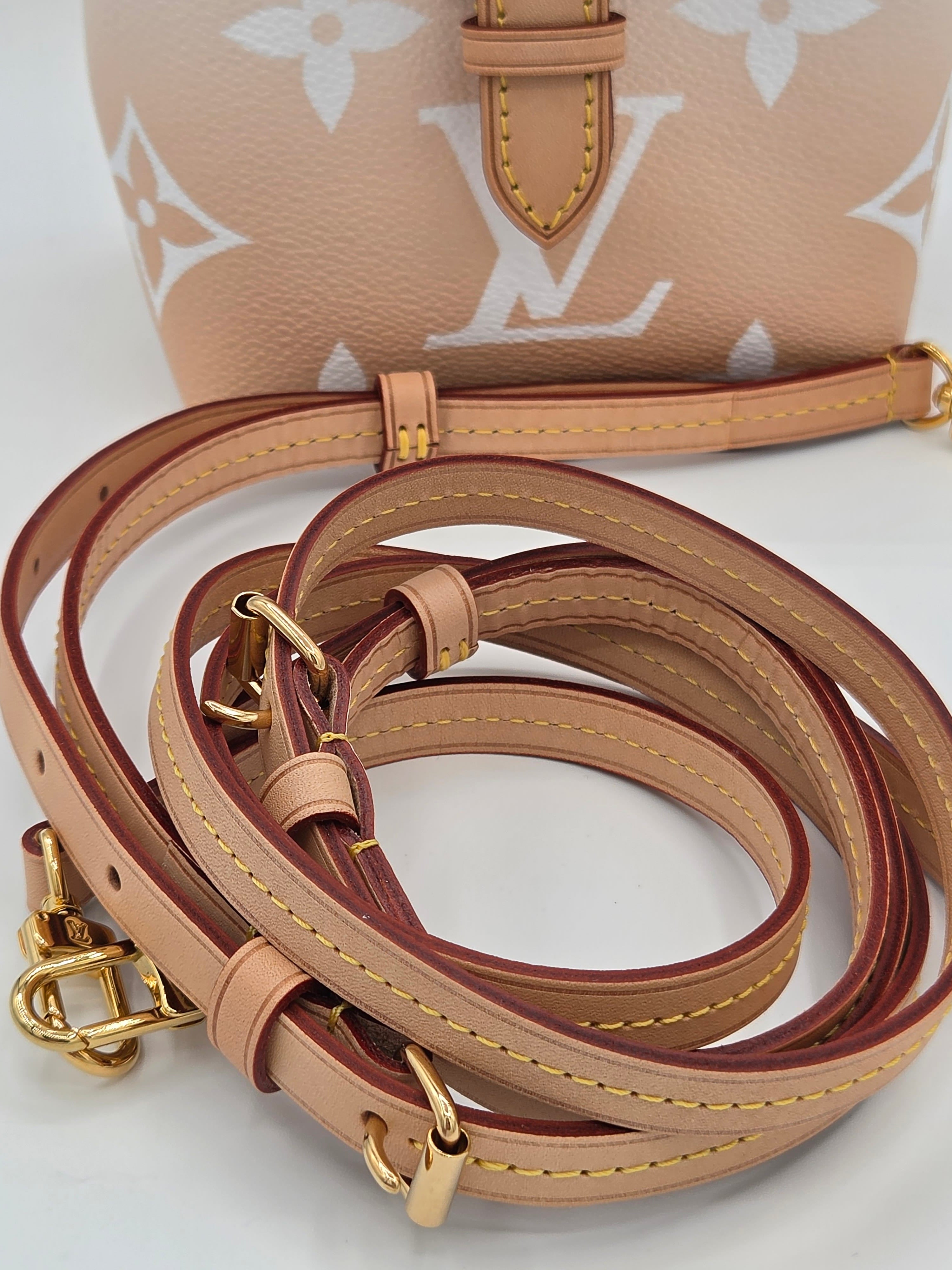 Close-up of a beige leather handbag strap with gold hardware on a light background