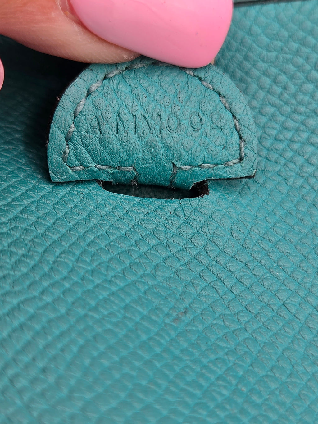 Close-up of a teal leather product with a brand label, held by a hand.