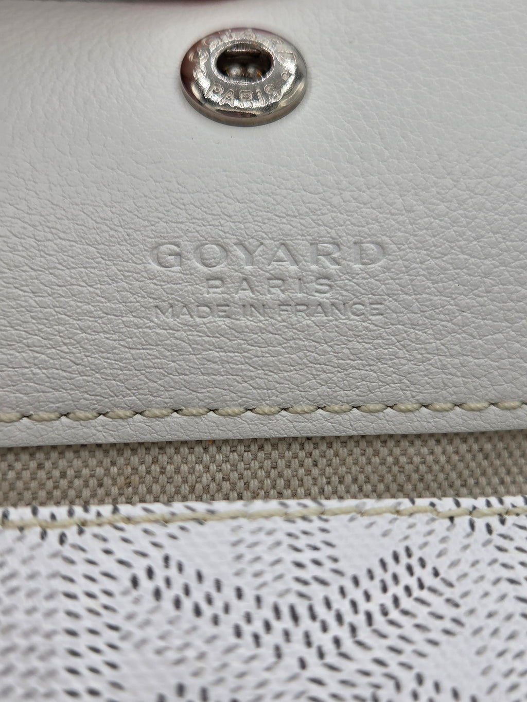 Close-up of a Goyard bag with leather texture and metal logo.