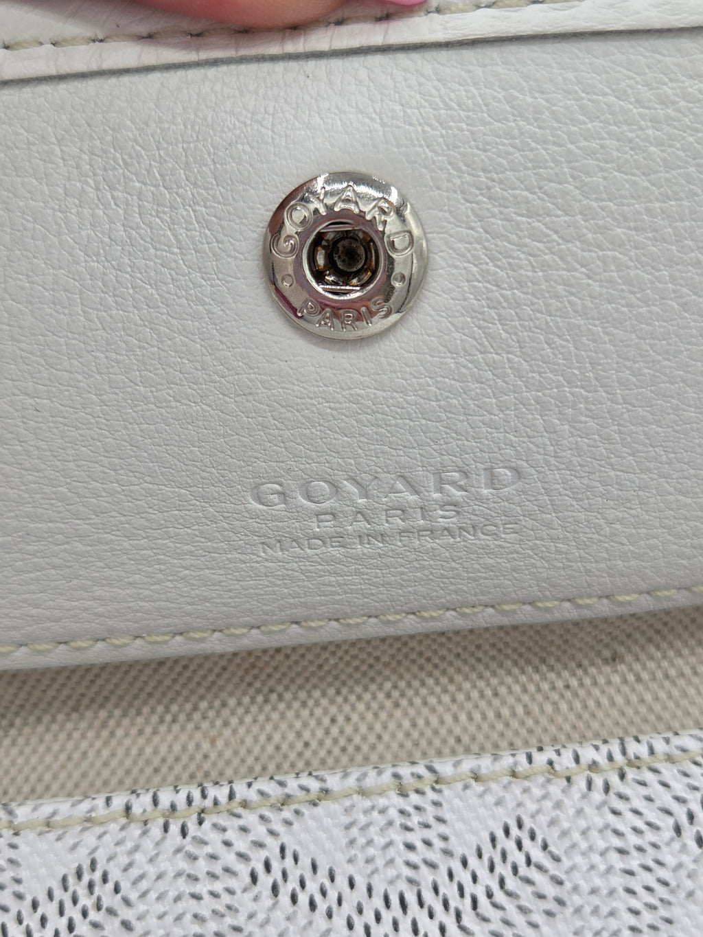 Close-up of a white leather bag with a metal button and 'Goyard' branding.