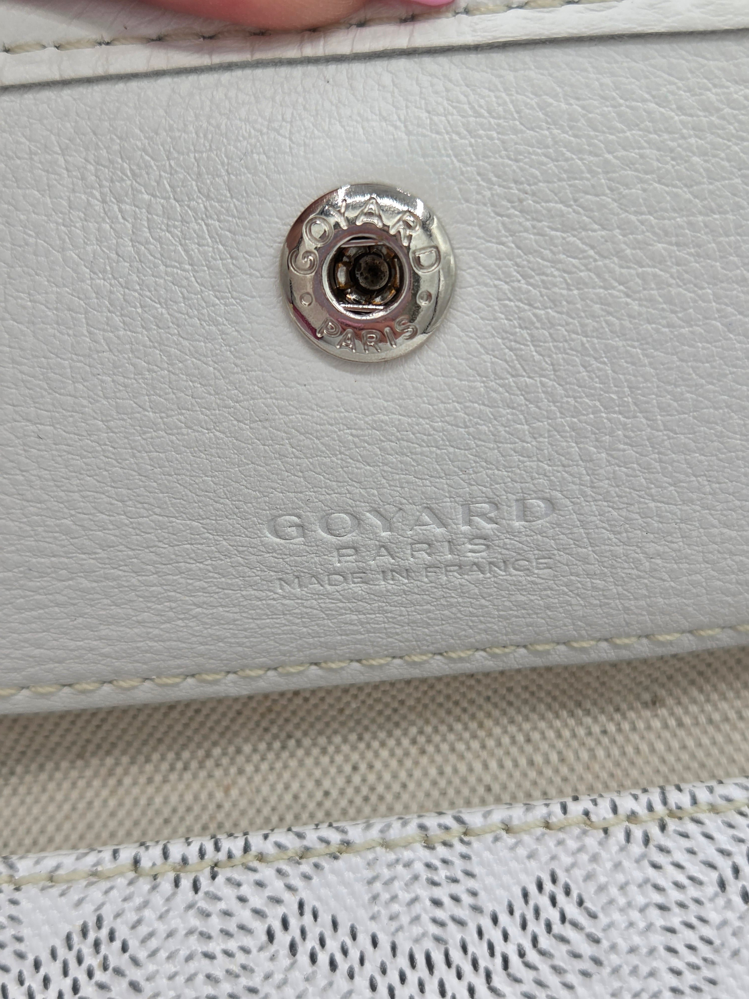 Close-up of a white leather bag with a metal button and 'Goyard' branding.