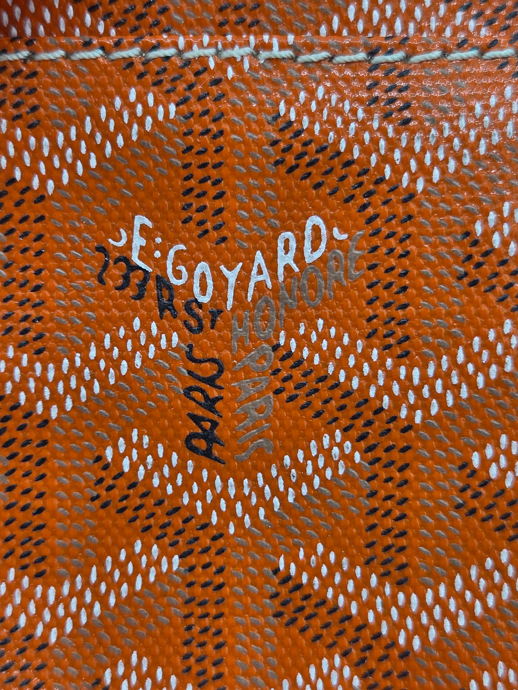 Close-up of a patterned fabric with 'Goyard' branding on an orange background.