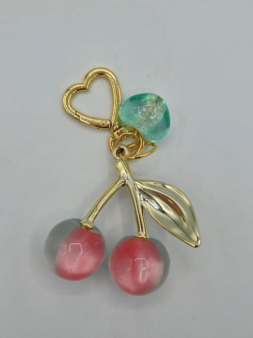 Jewelry piece with gold heart, green heart-shaped gem, and pink and gray beads on a light gray background