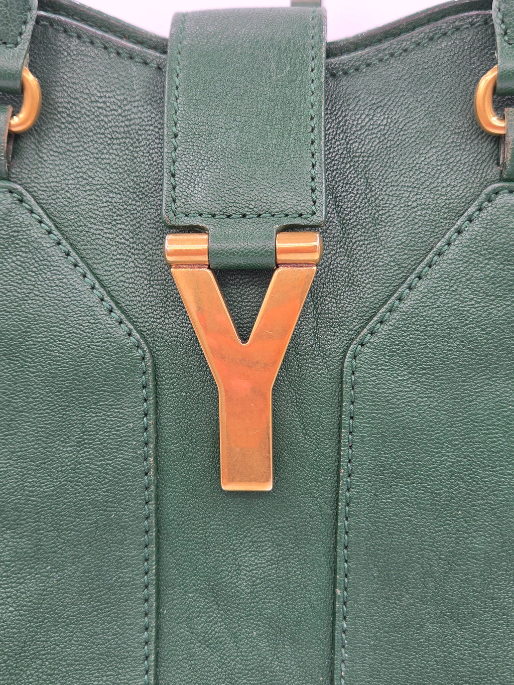 Green leather bag with a bronze buckle on a light purple background