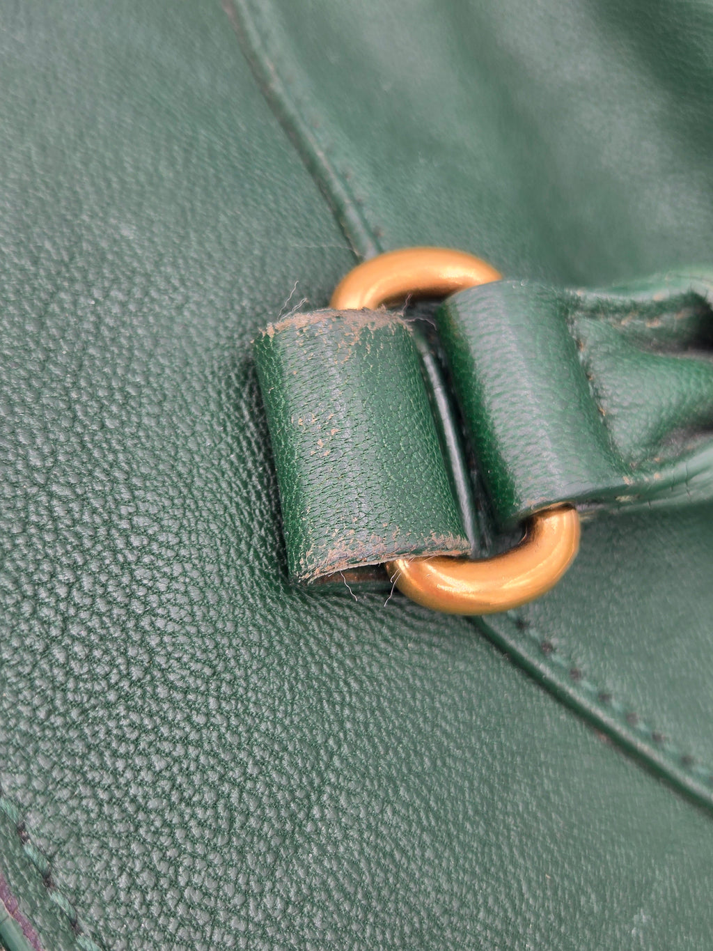 Close-up of a green leather bag with a gold buckle.