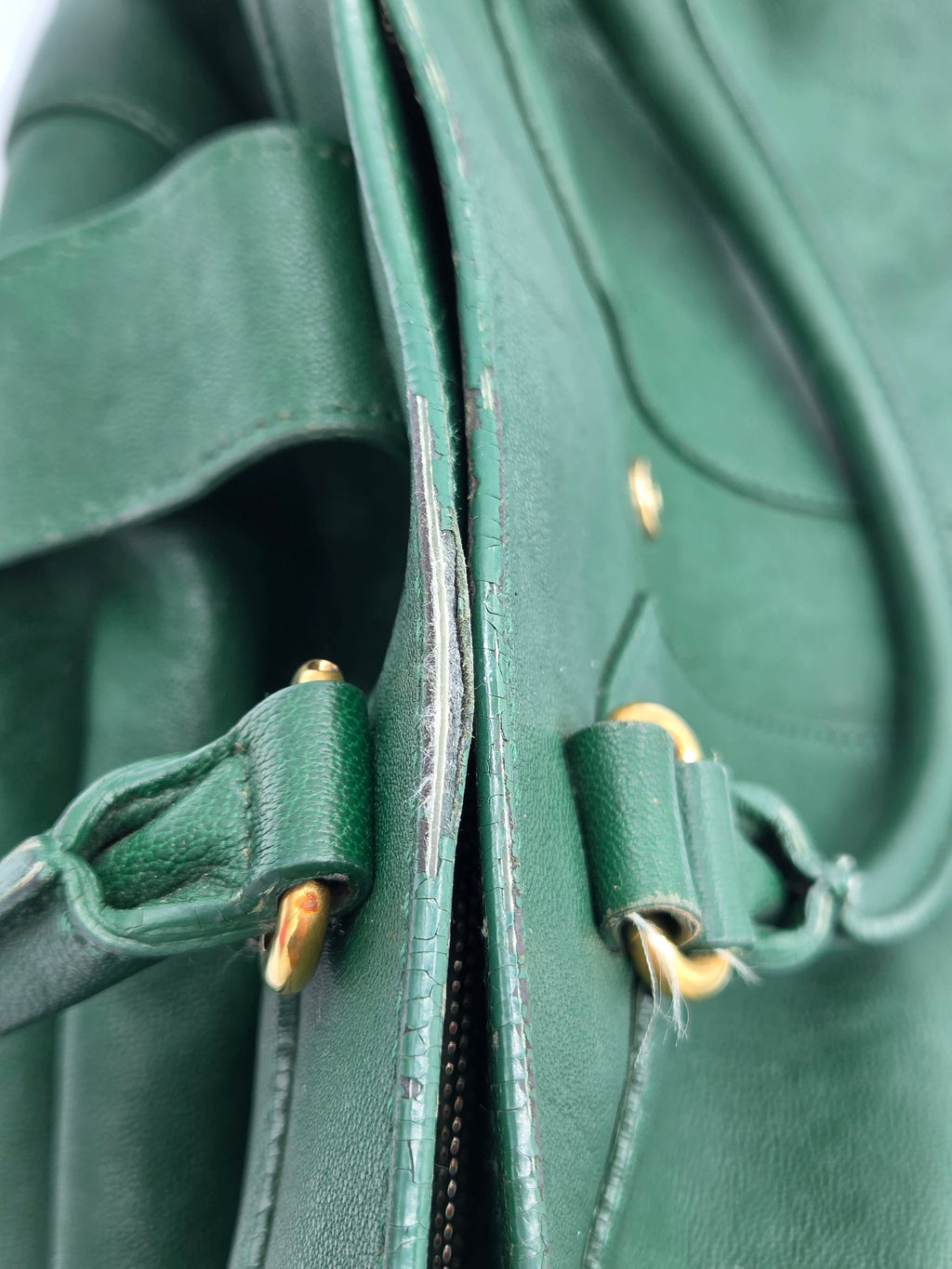 Close-up of a green leather bag with gold zipper pulls.