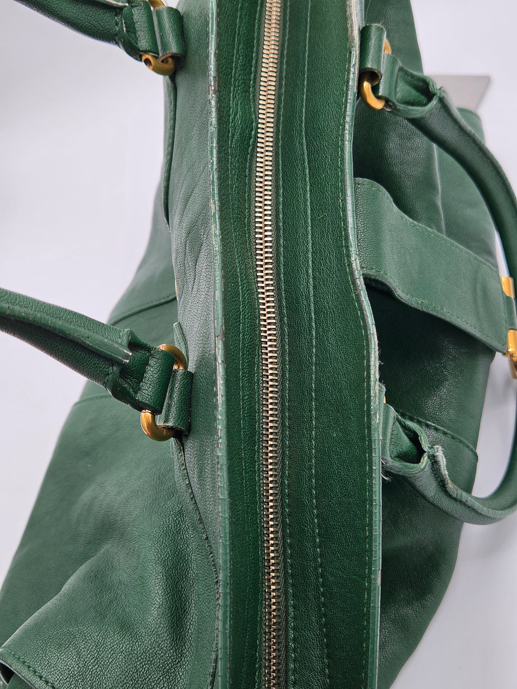 Close-up of a green bag with gold zippers and hardware on a white background
