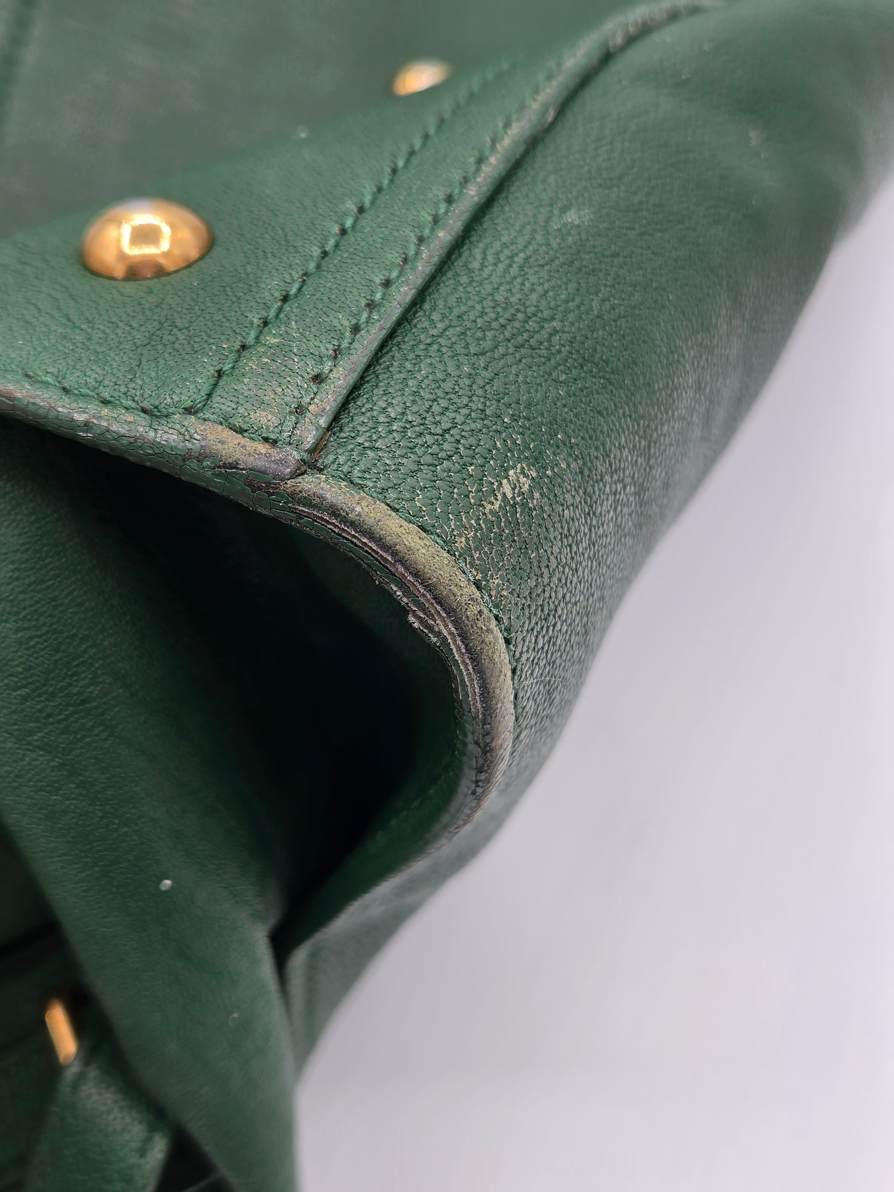 Close-up of a green leather bag with gold rivets on a light gray background