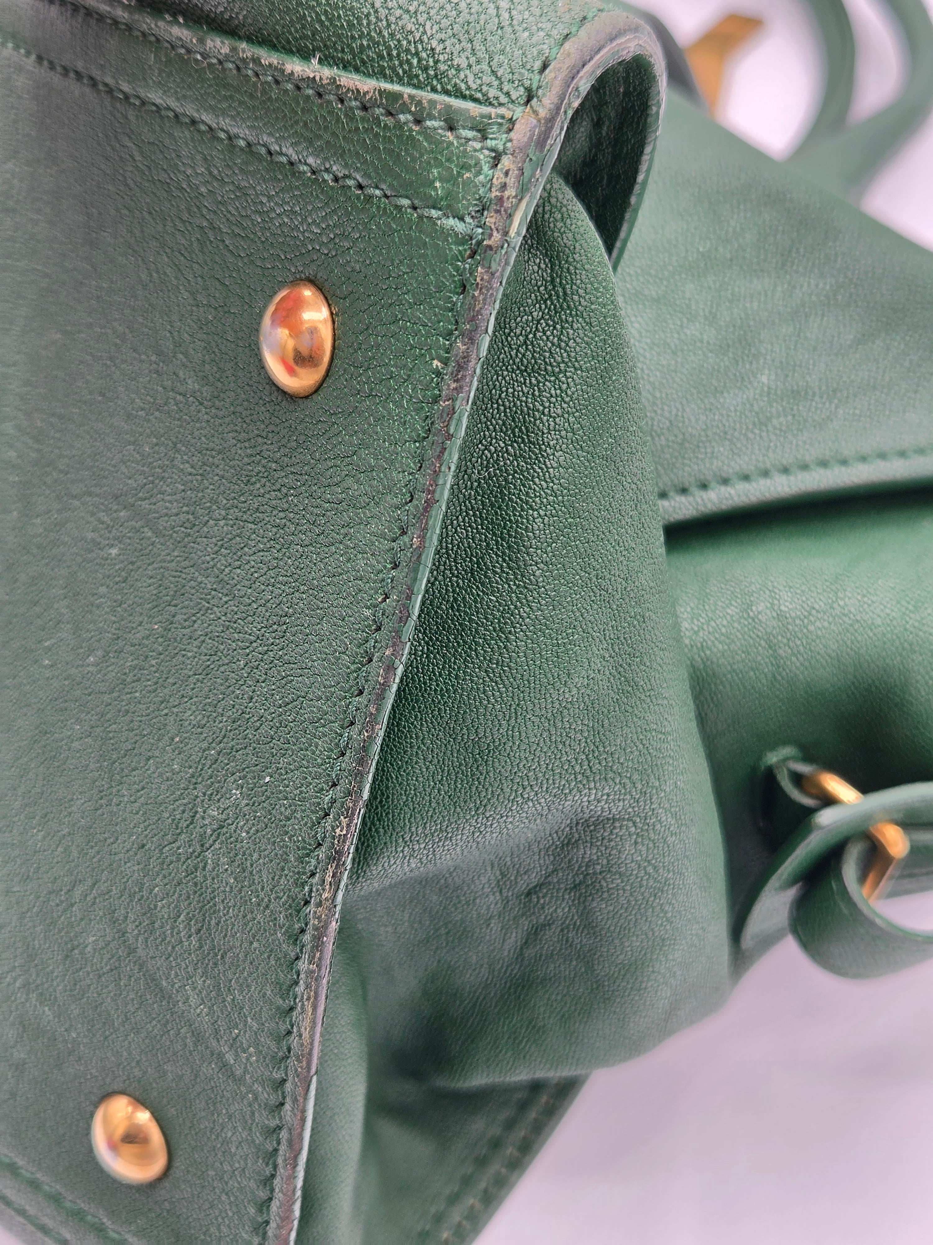 Close-up of a green leather handbag with gold rivets on a light gray background