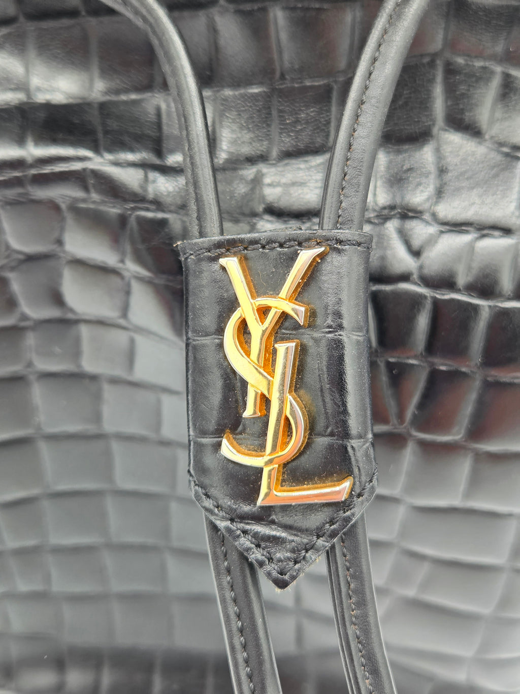 Close-up of a Yves Saint Laurent handbag with gold logo on gray textured background