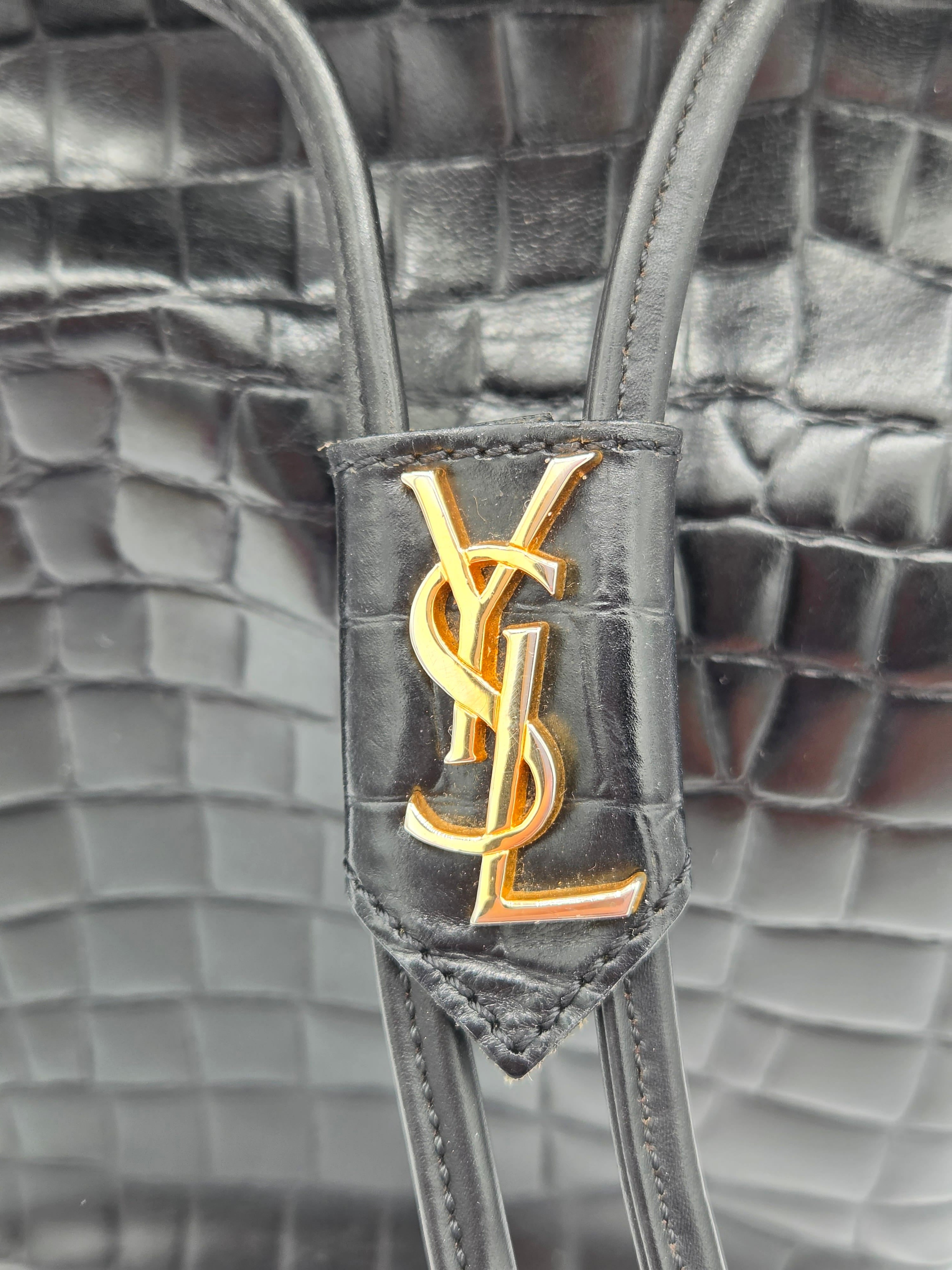 Close-up of a Yves Saint Laurent handbag with gold logo on gray textured background