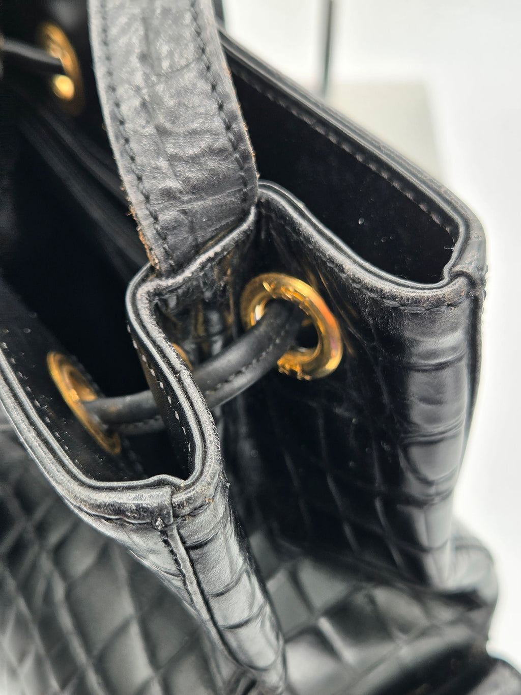 Close-up of a black quilted handbag with gold hardware on a light gray background