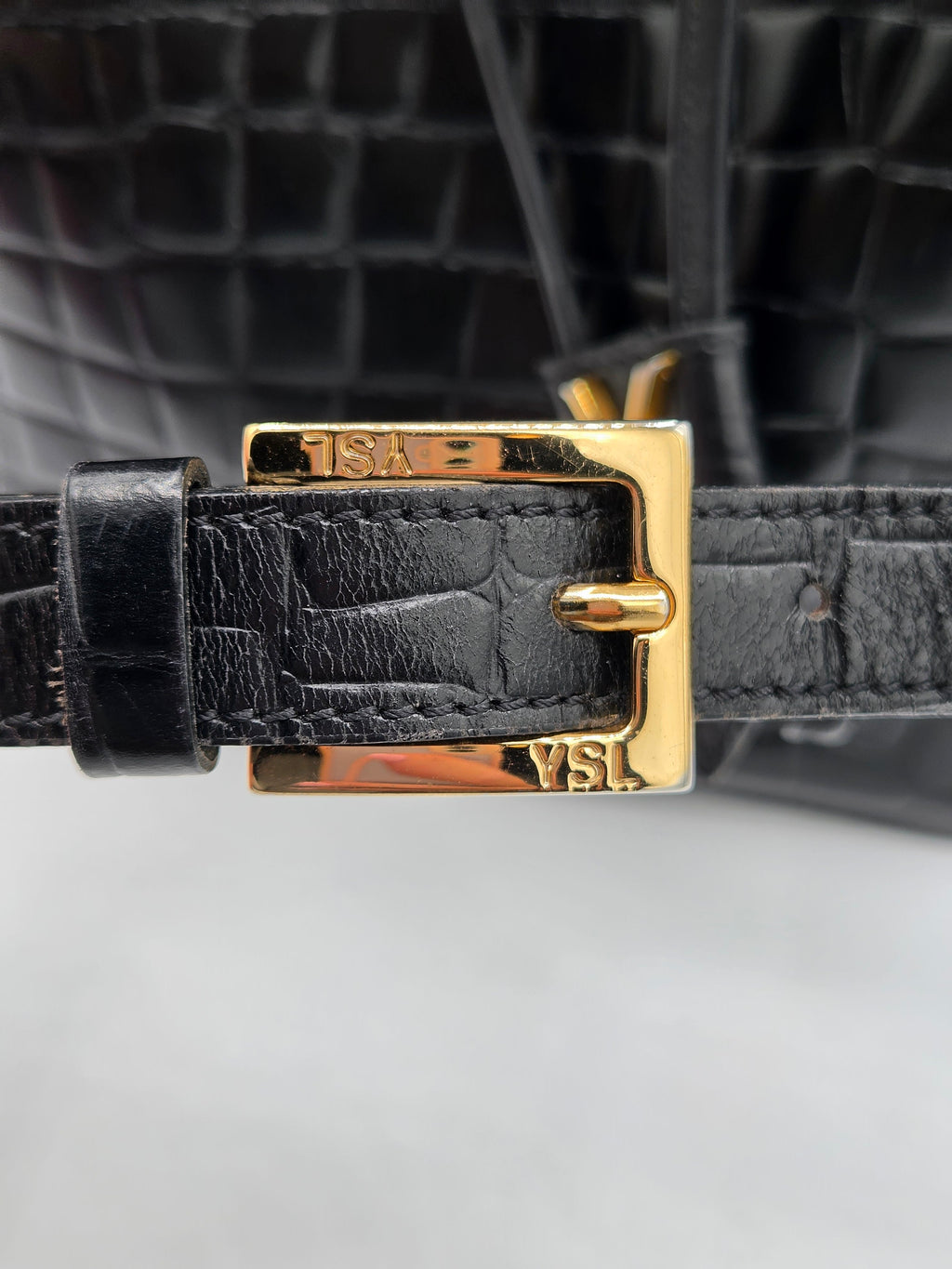 Close-up of a black leather strap with gold buckle on a blurred background