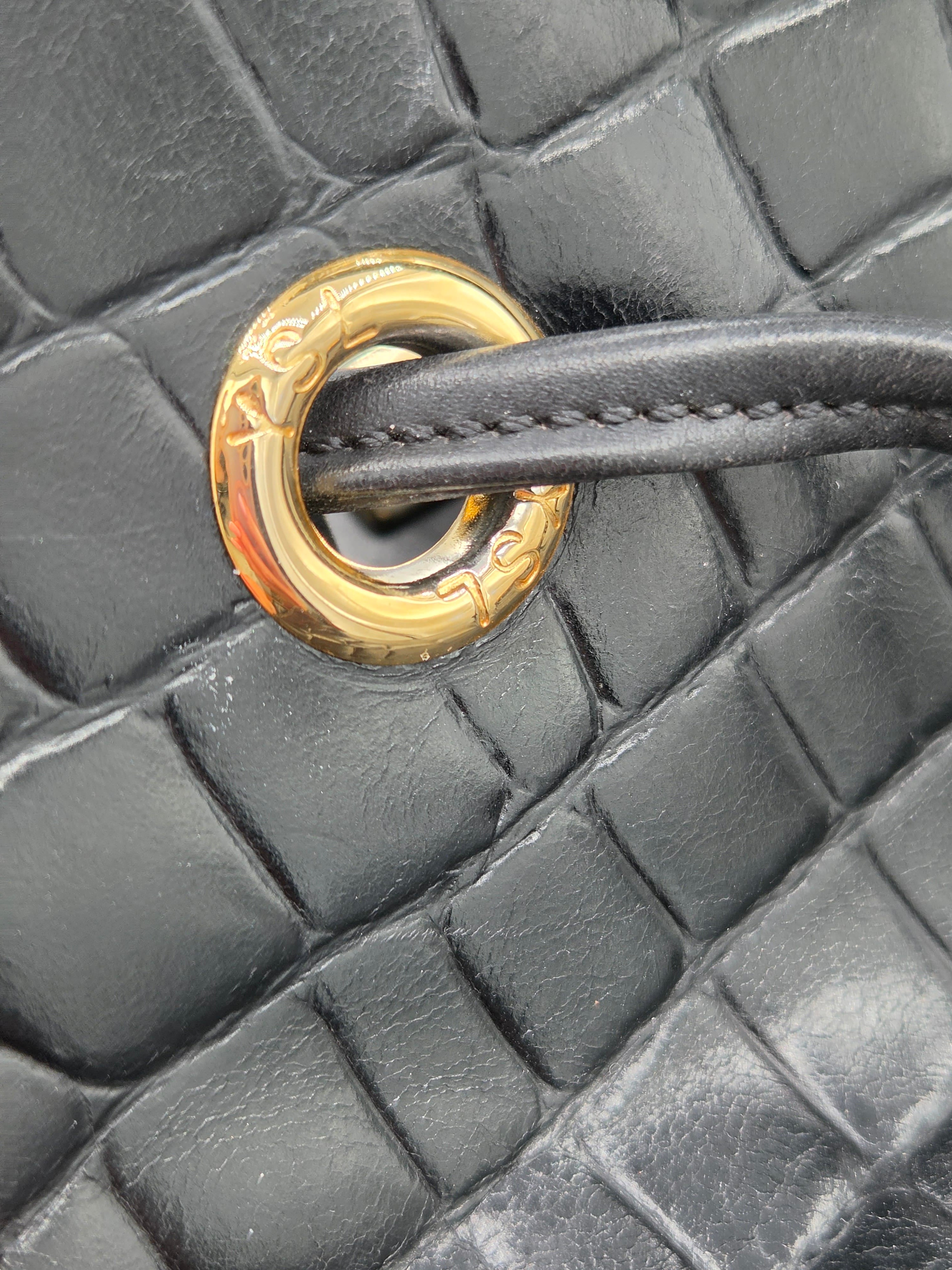 Close-up of a black textured handbag with a gold metal ring handle.
