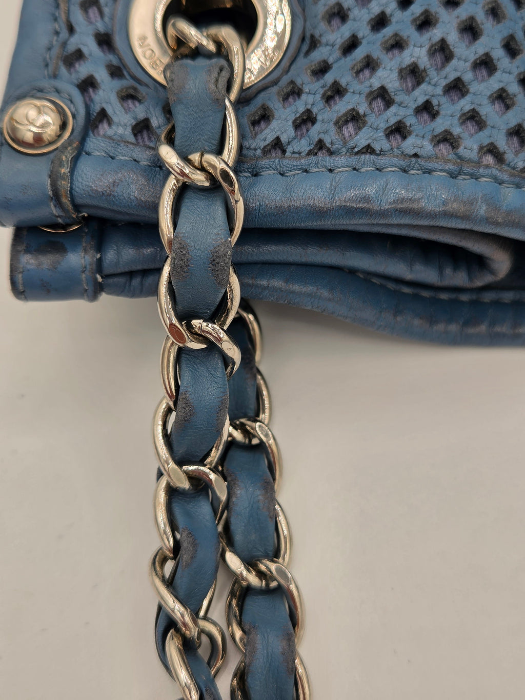 Close-up of a blue handbag with chain detail on a neutral background