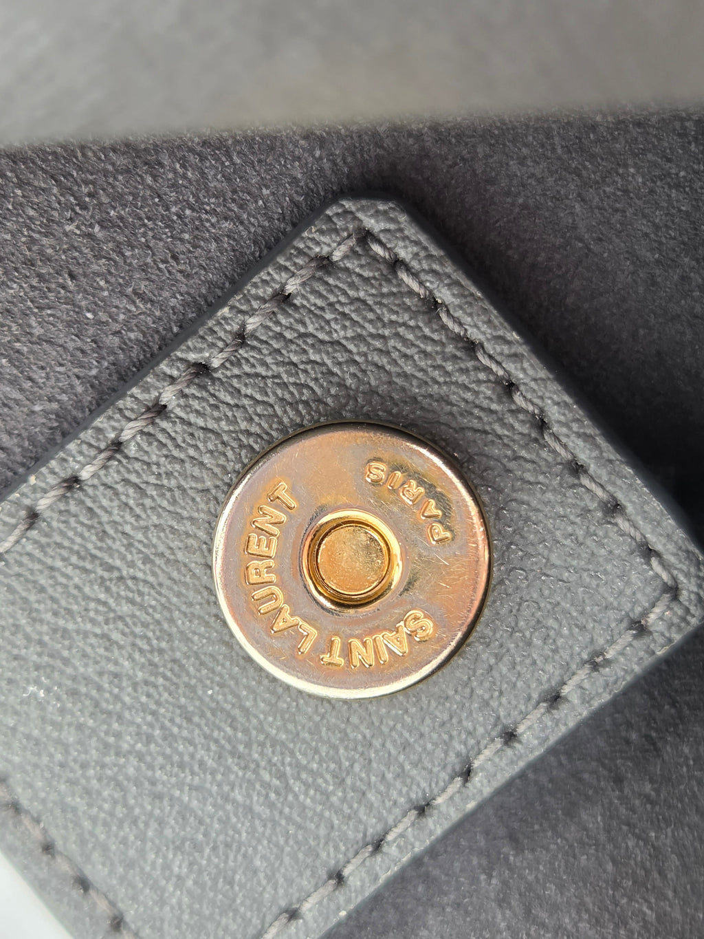 Close-up of a gray leather product with a gold button featuring 'Saint Laurent' branding.
