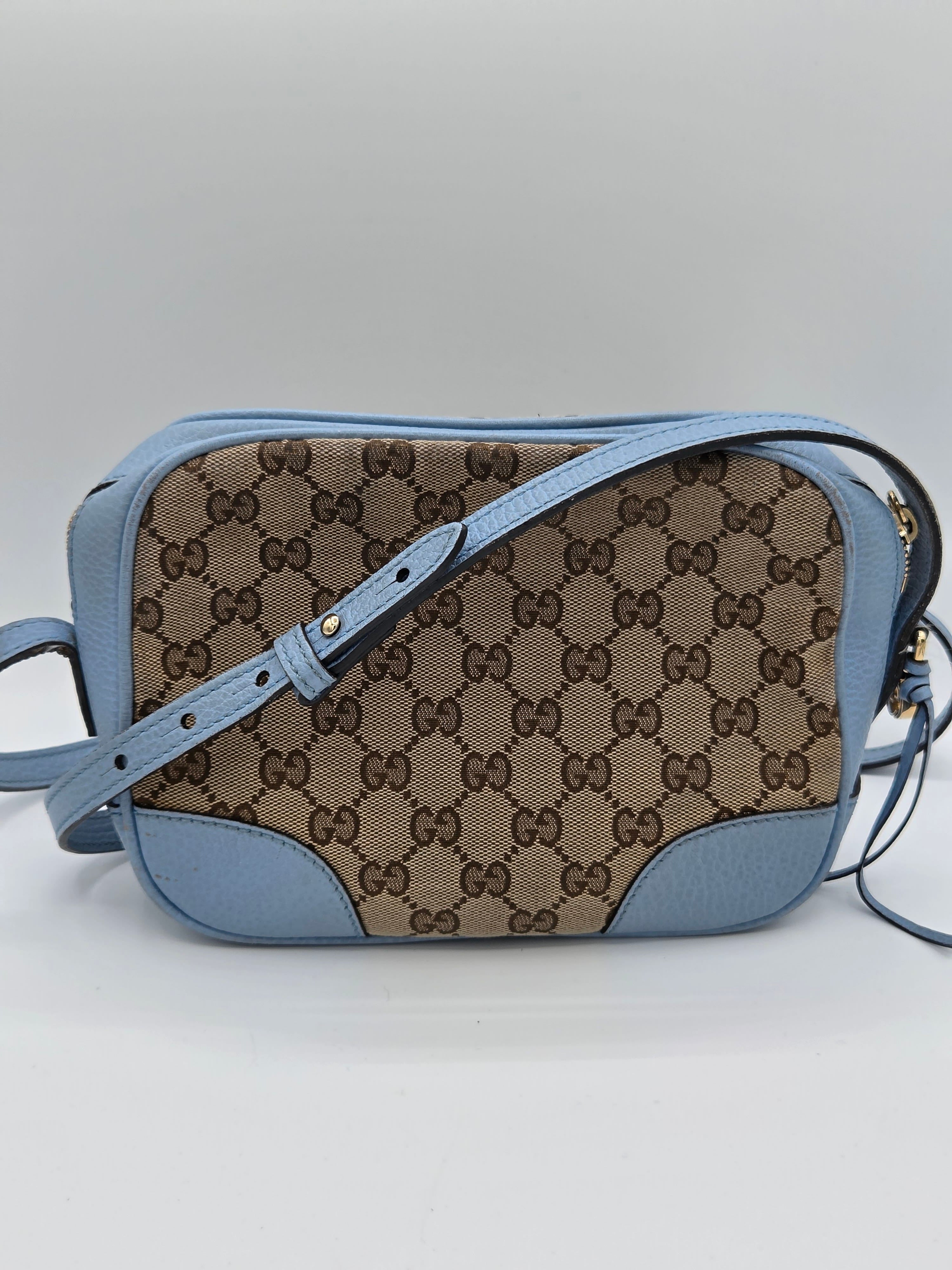 Designer handbag with patterned flap and blue strap on a light gray background
