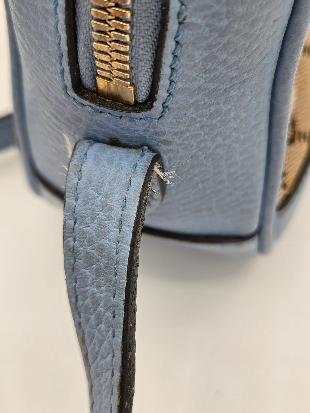 Close-up of a blue leather bag with a gold zipper on a light background