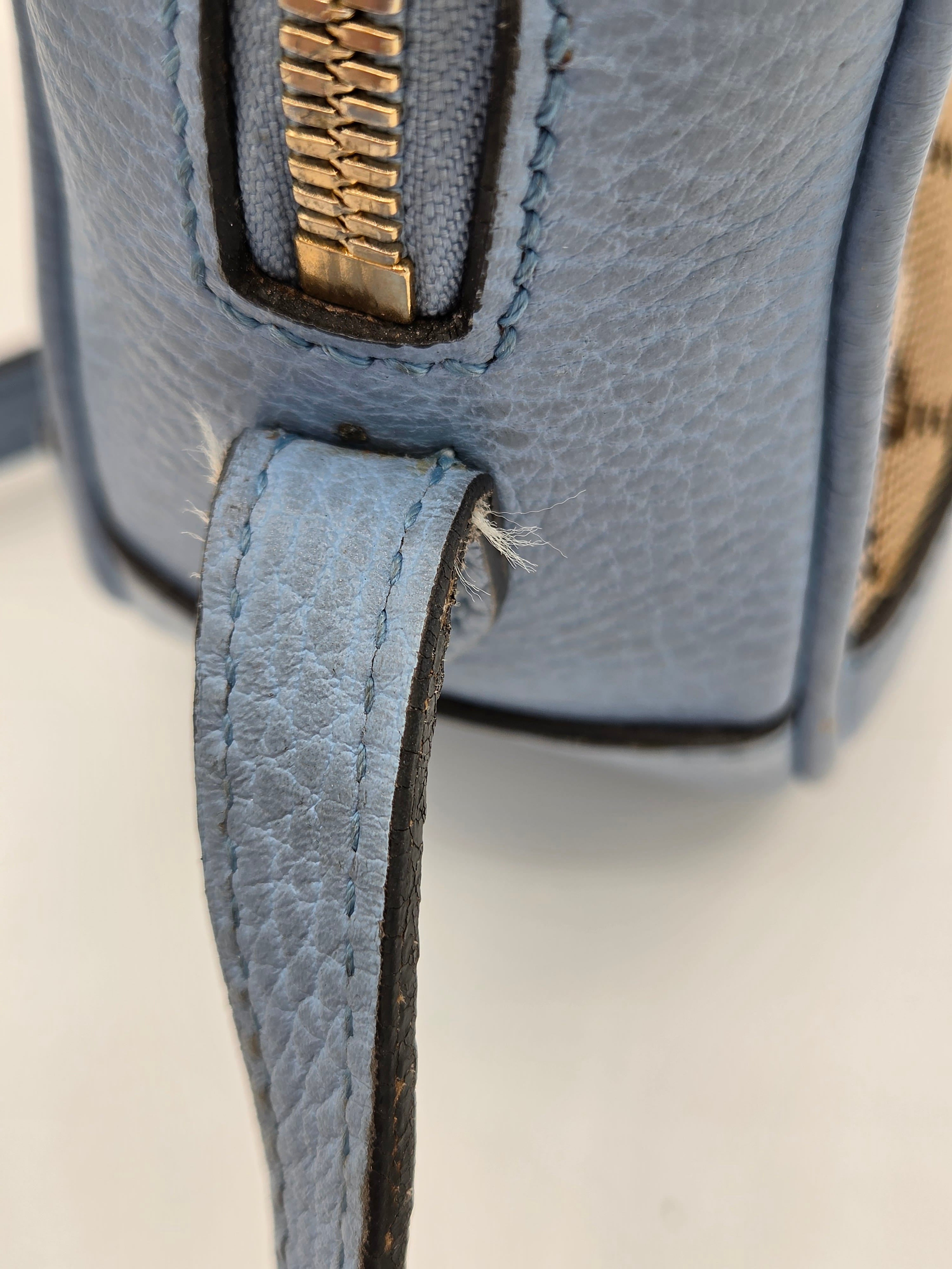 Close-up of a blue leather bag with a gold zipper on a light background