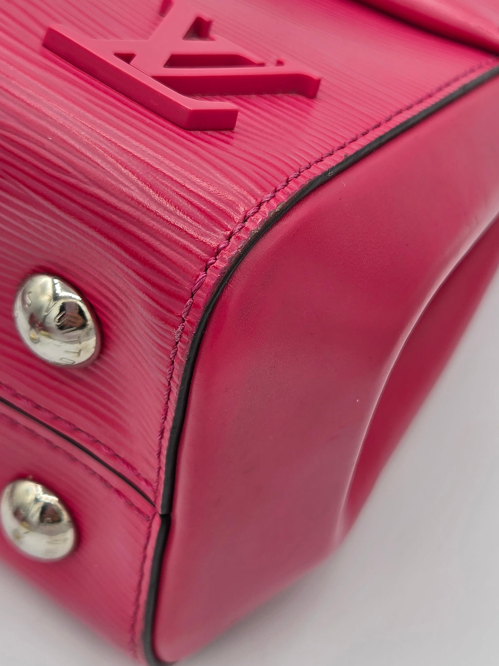 Close-up of a pink handbag with a brand logo and silver studs on a white background
