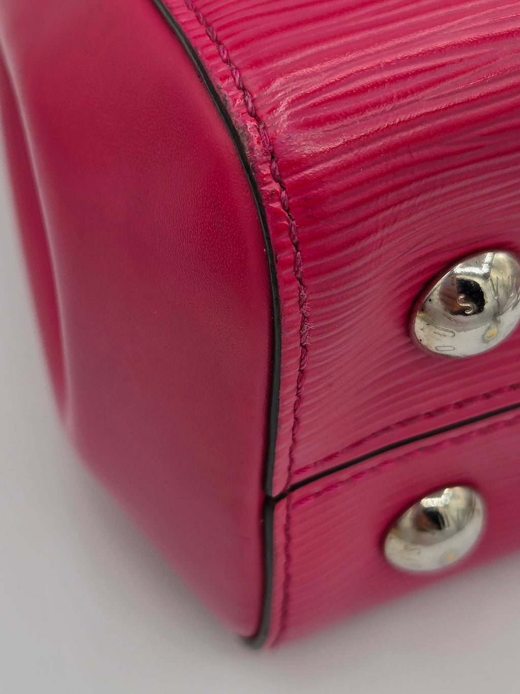 Close-up of a pink textured handbag with metal studs on a white background