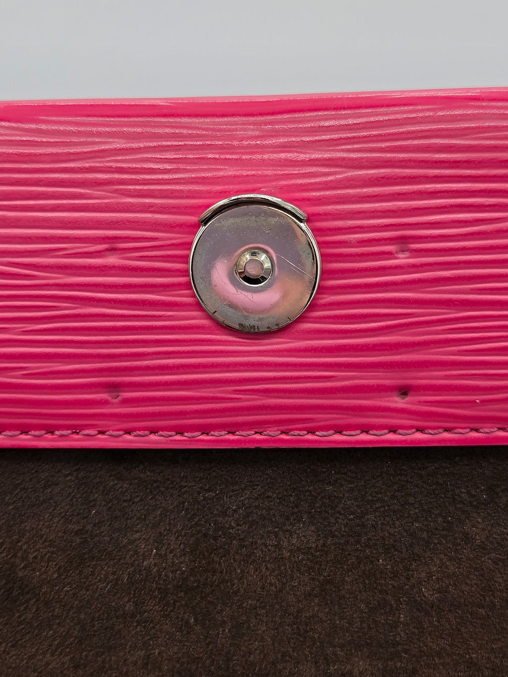 Close-up of a pink textured surface with a metal button and brown fabric.