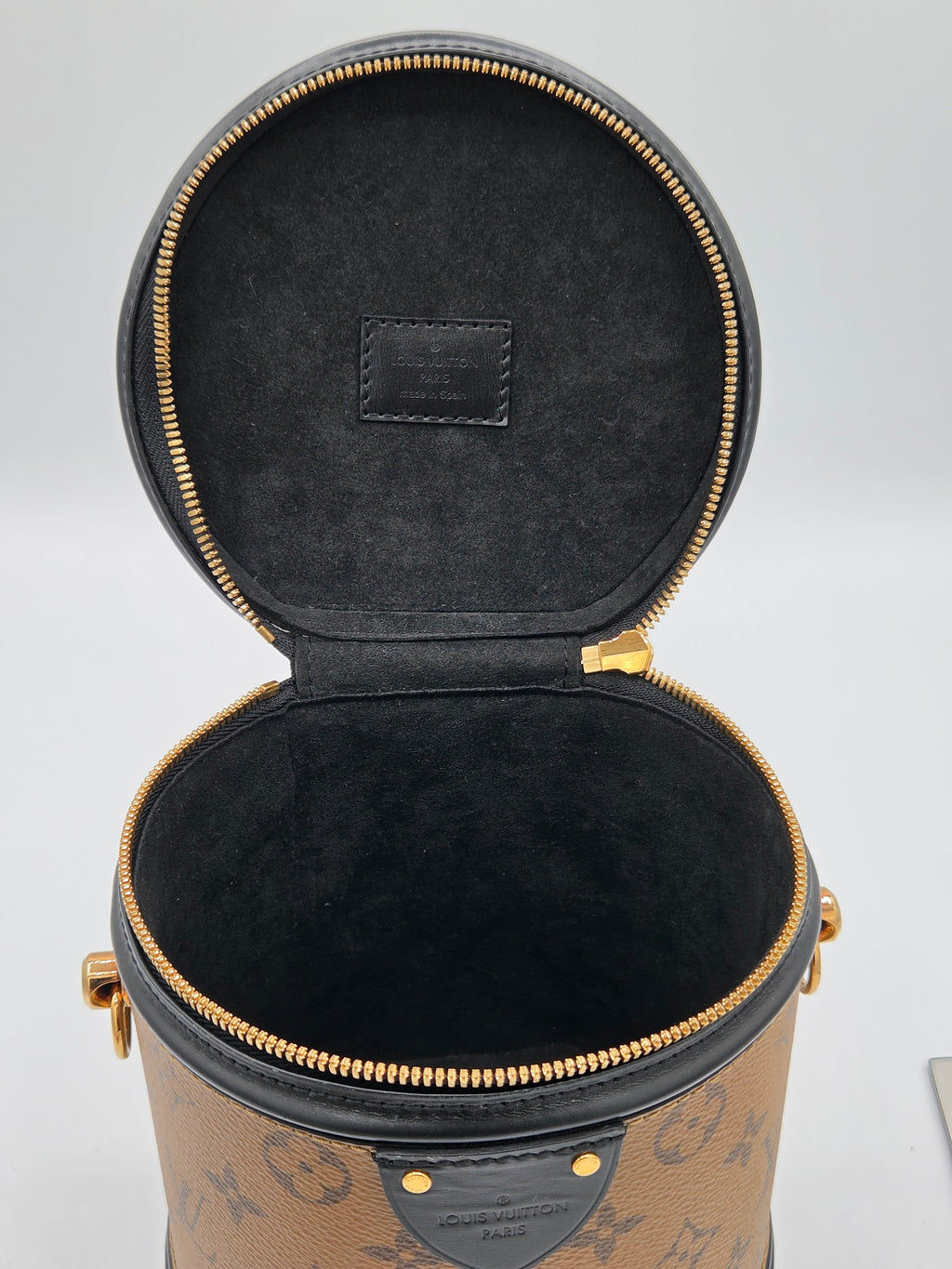 Open cylindrical black leather case with gold zipper on a light gray background