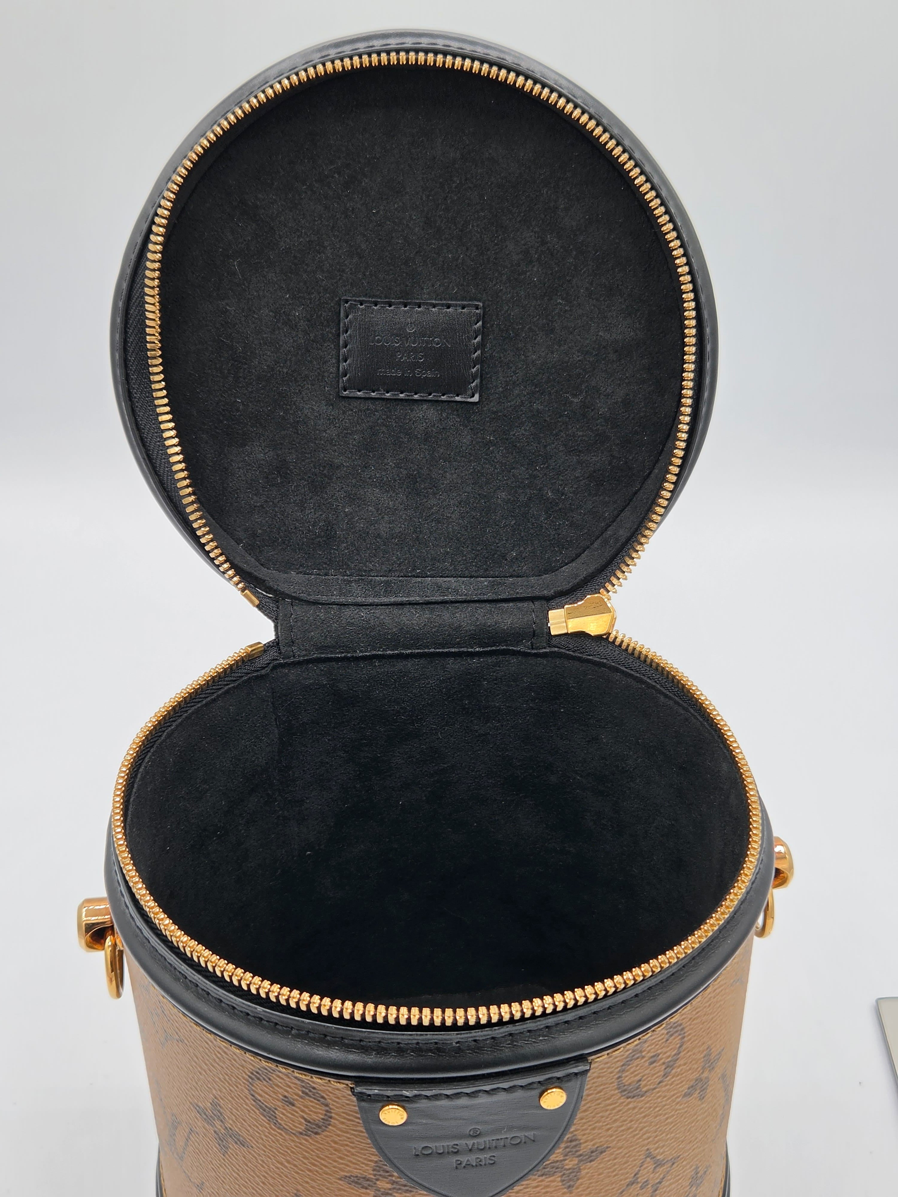Open cylindrical black leather case with gold zipper on a light gray background