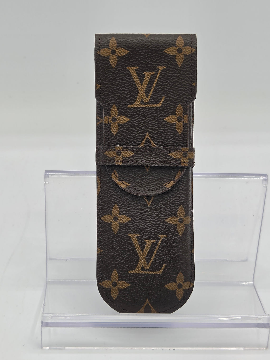 Louis Vuitton monogram canvas belt shown flat against a white background, with a clear acrylic display block behind it.