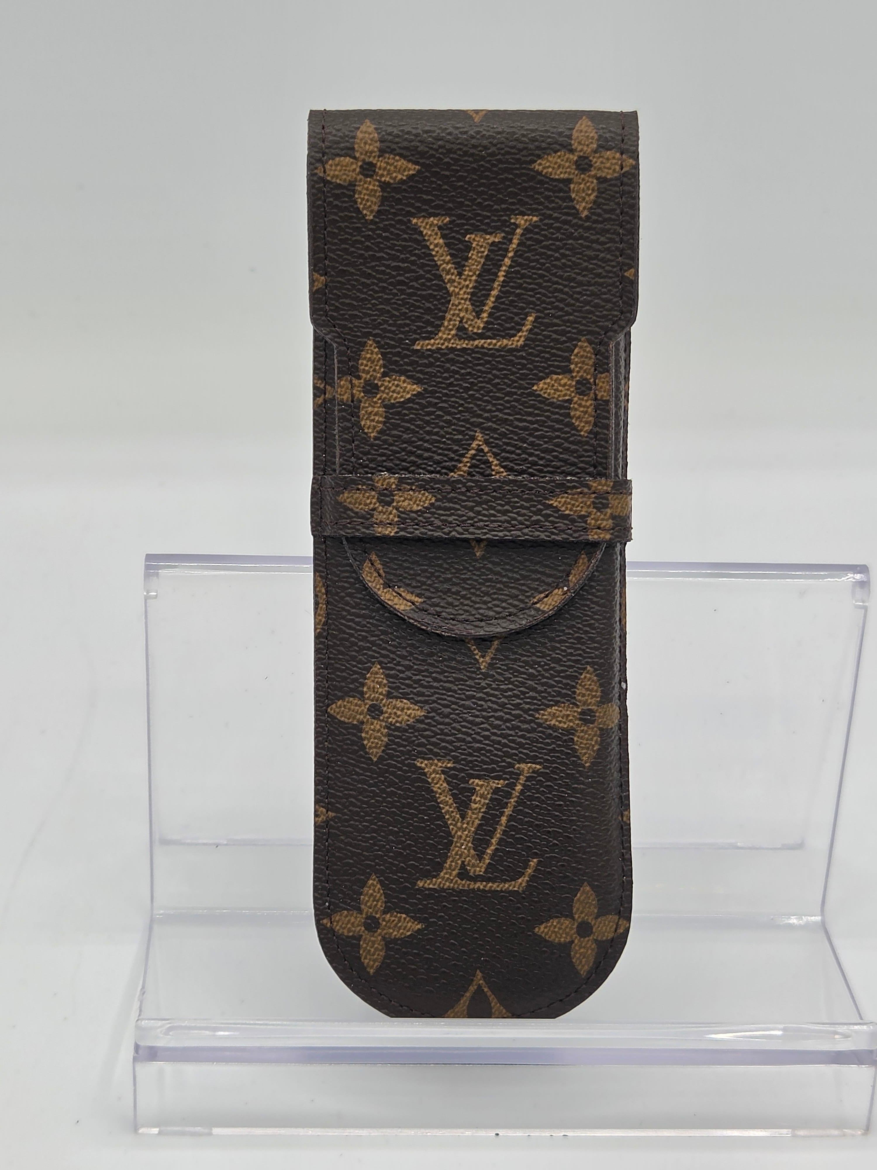 Louis Vuitton monogram canvas belt shown flat against a white background, with a clear acrylic display block behind it.