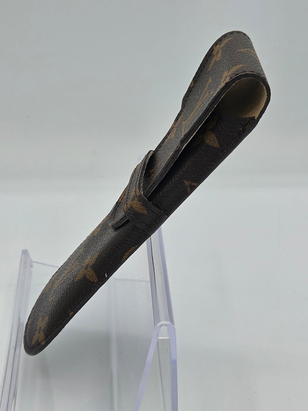 A single Louis Vuitton monogram leather shoe cover or sleeve displayed on a clear acrylic stand against a light gray background.