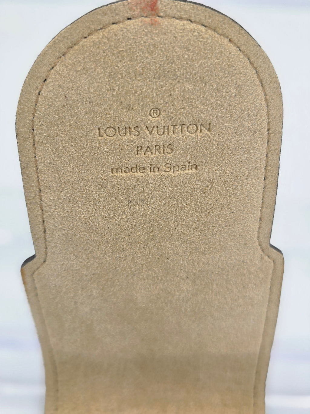 Close-up of a Louis Vuitton sandal insole showing the printed brand name 'LOUIS VUITTON PARIS' and 'made in Spain' on a beige suede-like surface.