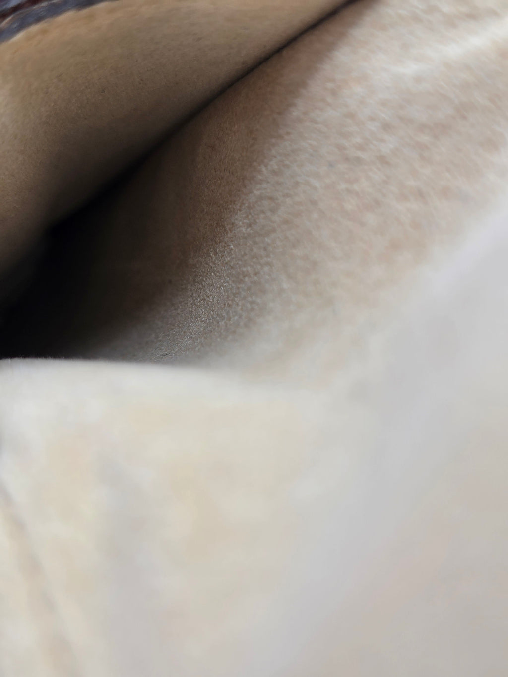 Close-up of a soft, plush fabric texture in a light beige or cream color, showing the material's fine pile and folds.